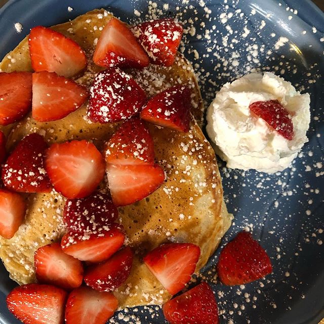 Buttermilk pancakes topped with fresh strawberries, powdered sugar, and whipped cream