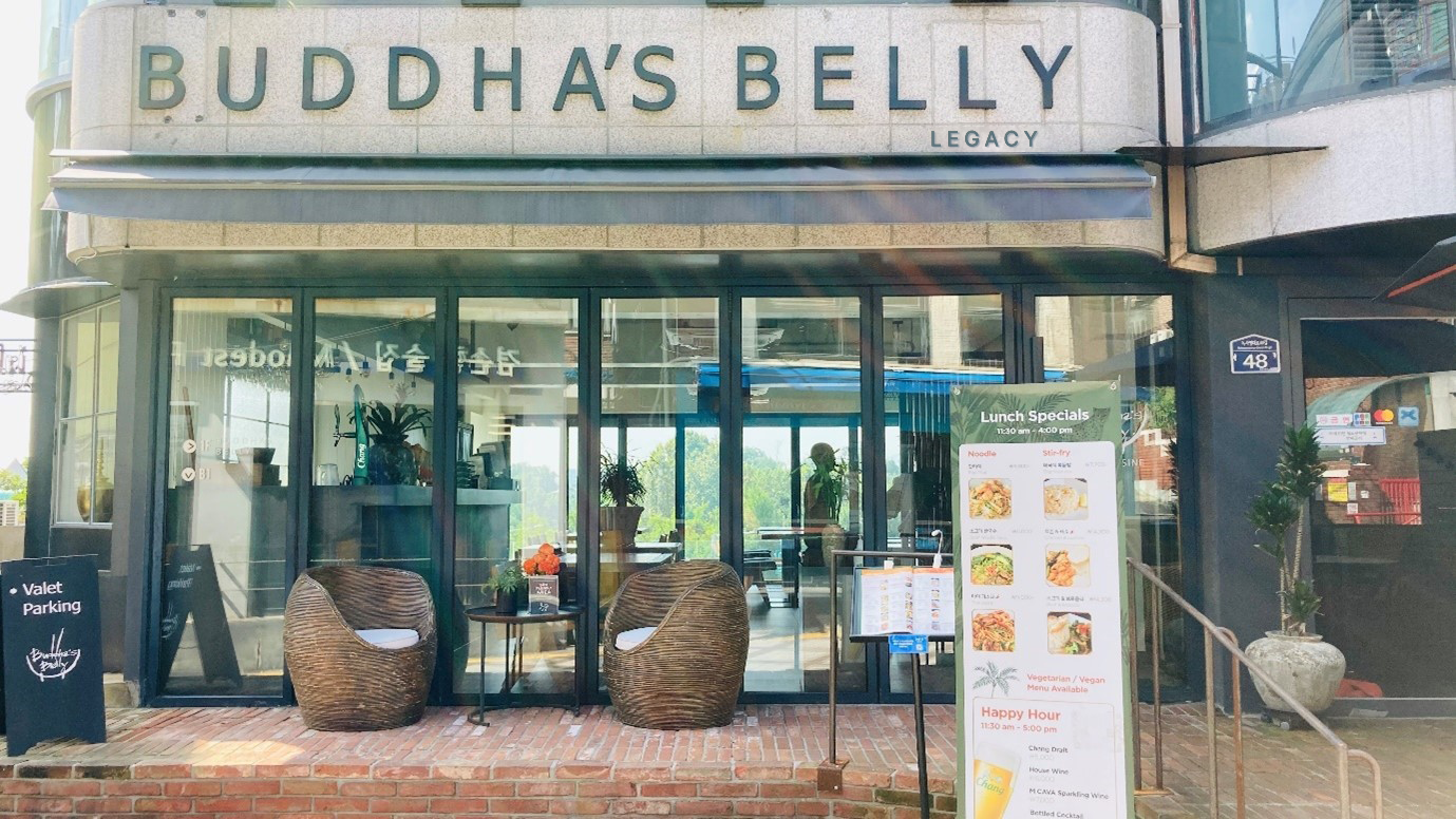Exterior facade and terrace entrance of Buddha's Belly Legacy with stone signage and rattan armchairs