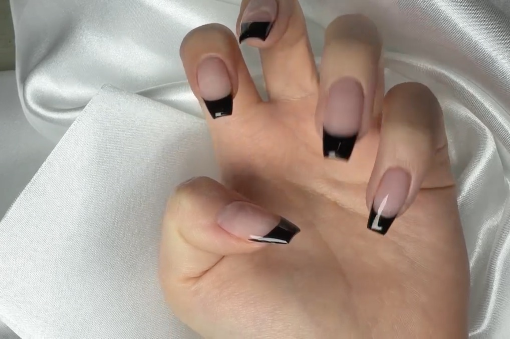 Hand showing classic black French tip manicure on coffin-shaped nails against white satin background