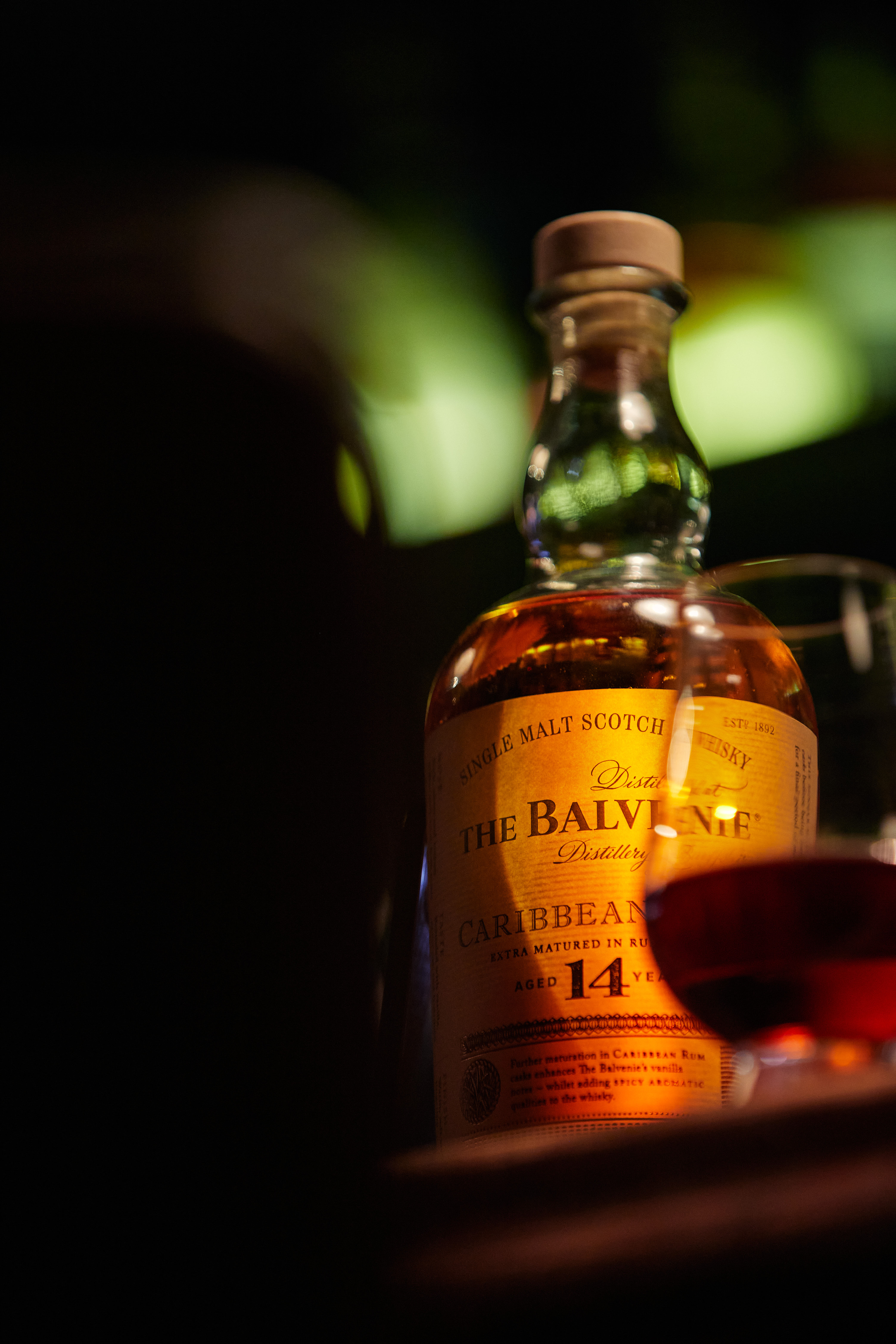Bottle of The Balvenie 14 Year Old Caribbean Cask illuminated against dark bar woodwork.