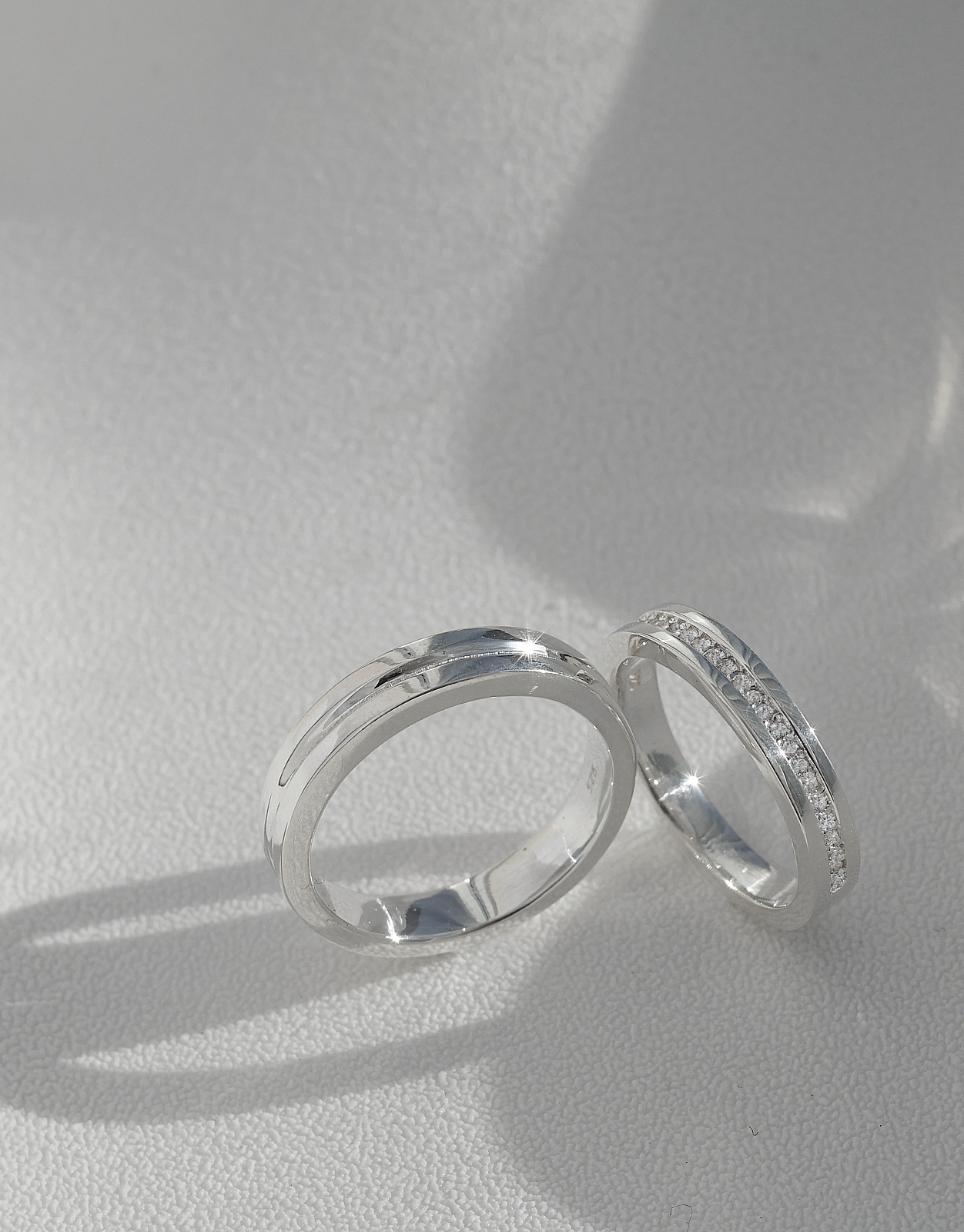 Pair of hand-finished silver rings resting in natural sunlight showing polished luster and precision pavé accents