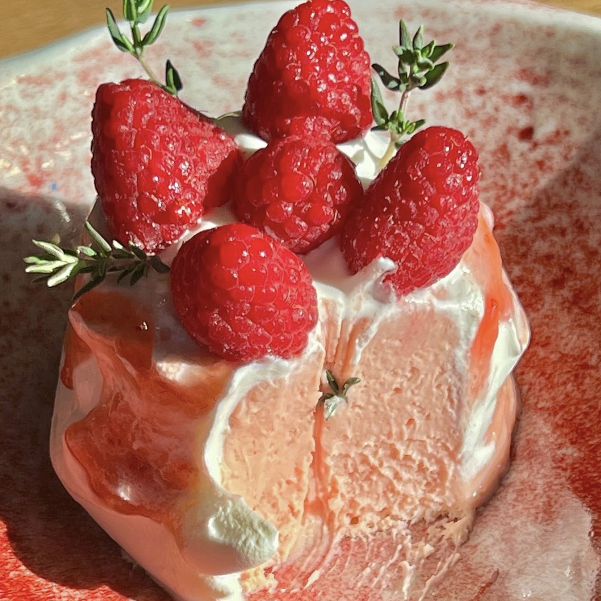 Pink berry mousse dessert topped with fresh raspberries and green herbs