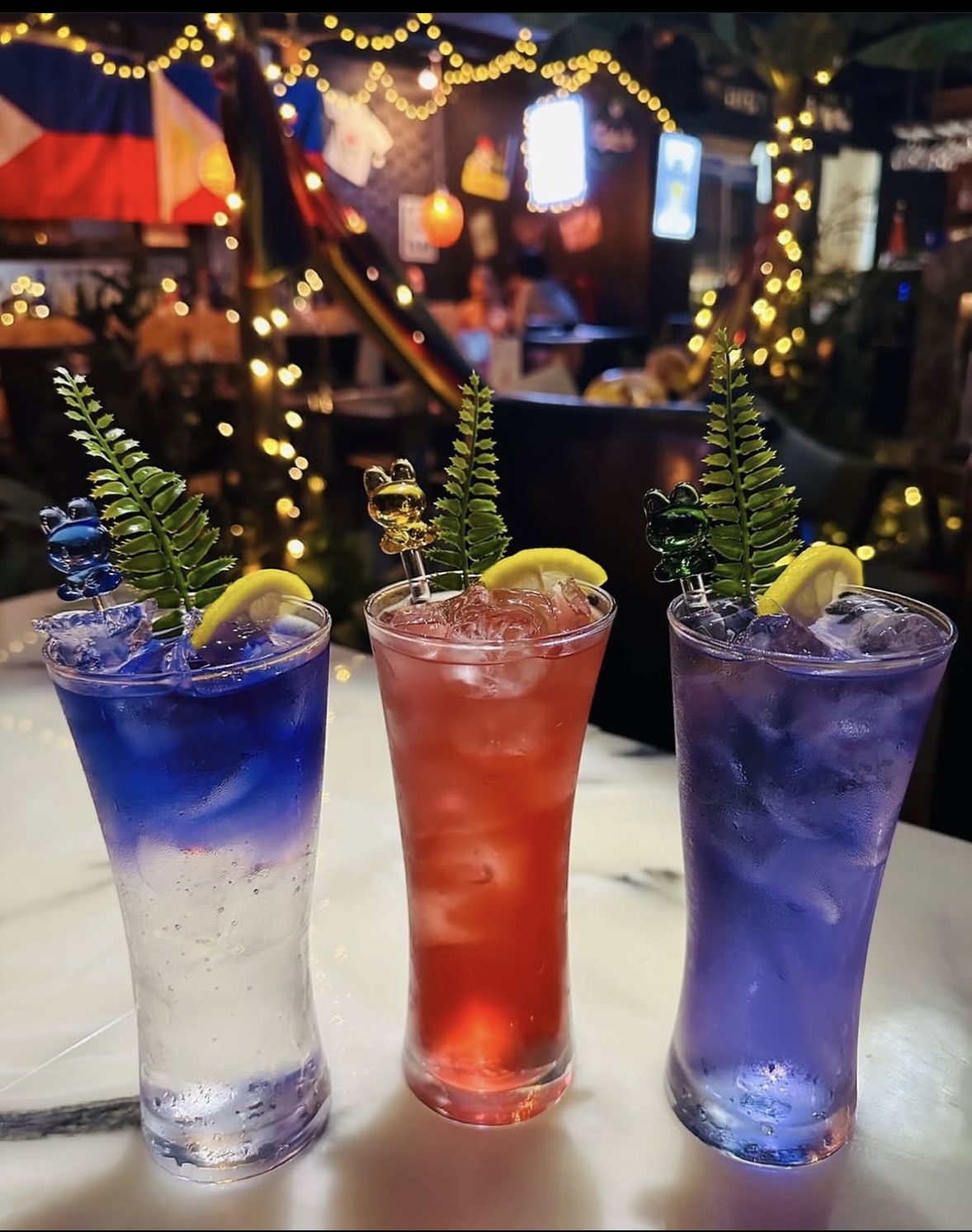 Signature colorful cocktails in tall glasses garnished with lemon and fern sprigs