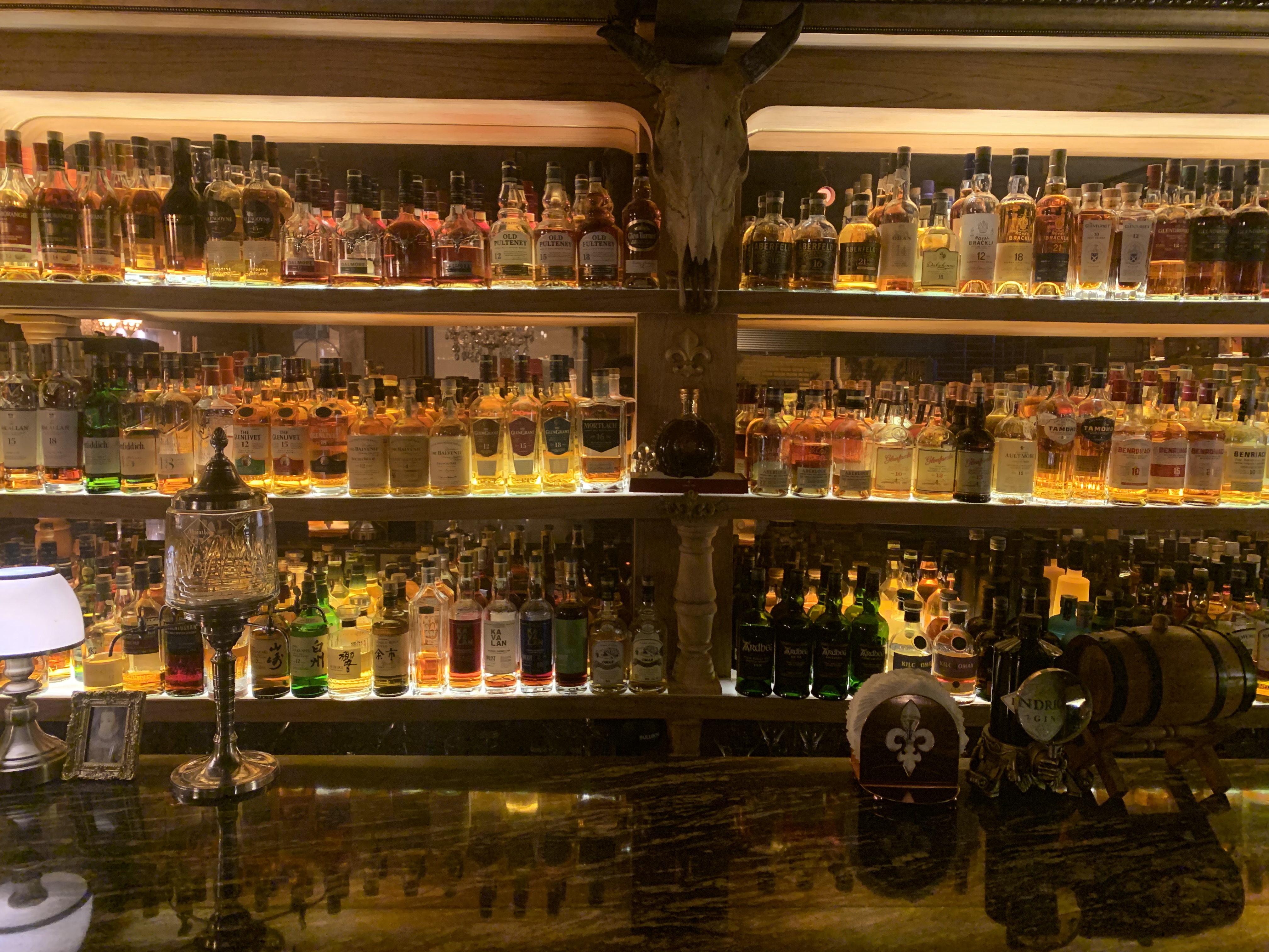 Backlit three-tiered shelves lined with whisky bottles at Dusk Till Dawn
