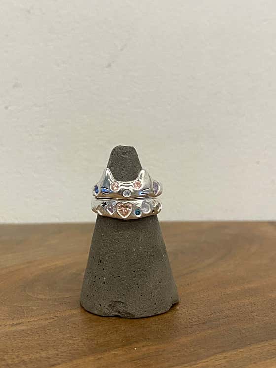 Two stacked silver rings with decorative stones displayed on a grey cone stand
