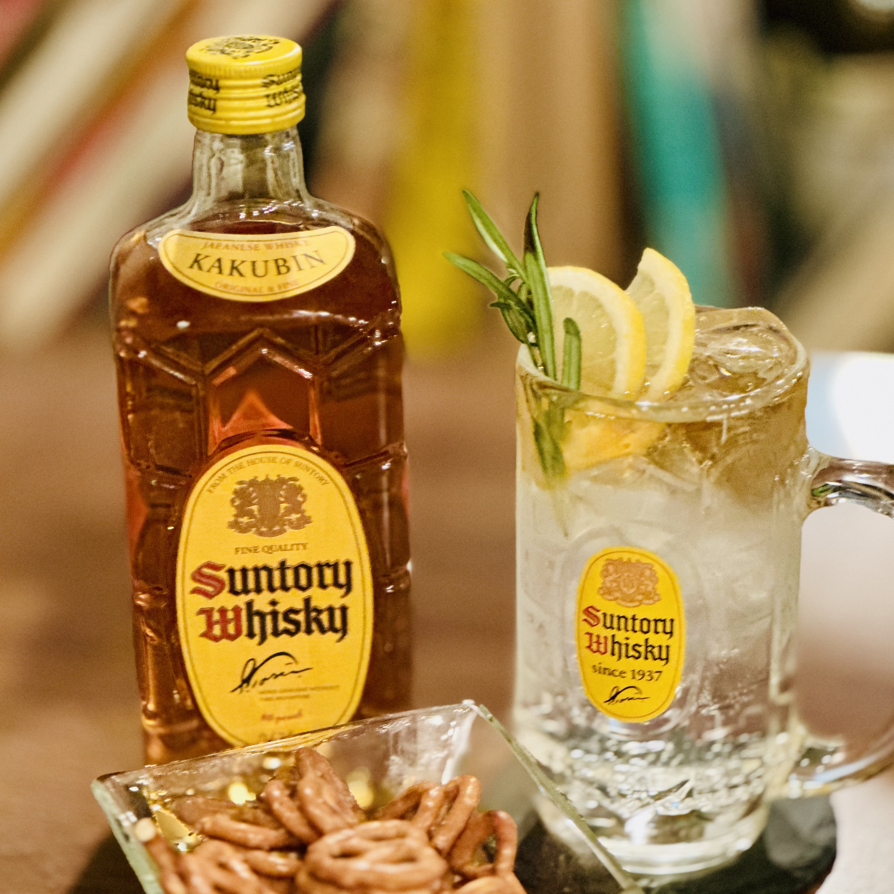 A bottle of Suntory whisky next to a highball glass with lemon and rosemary