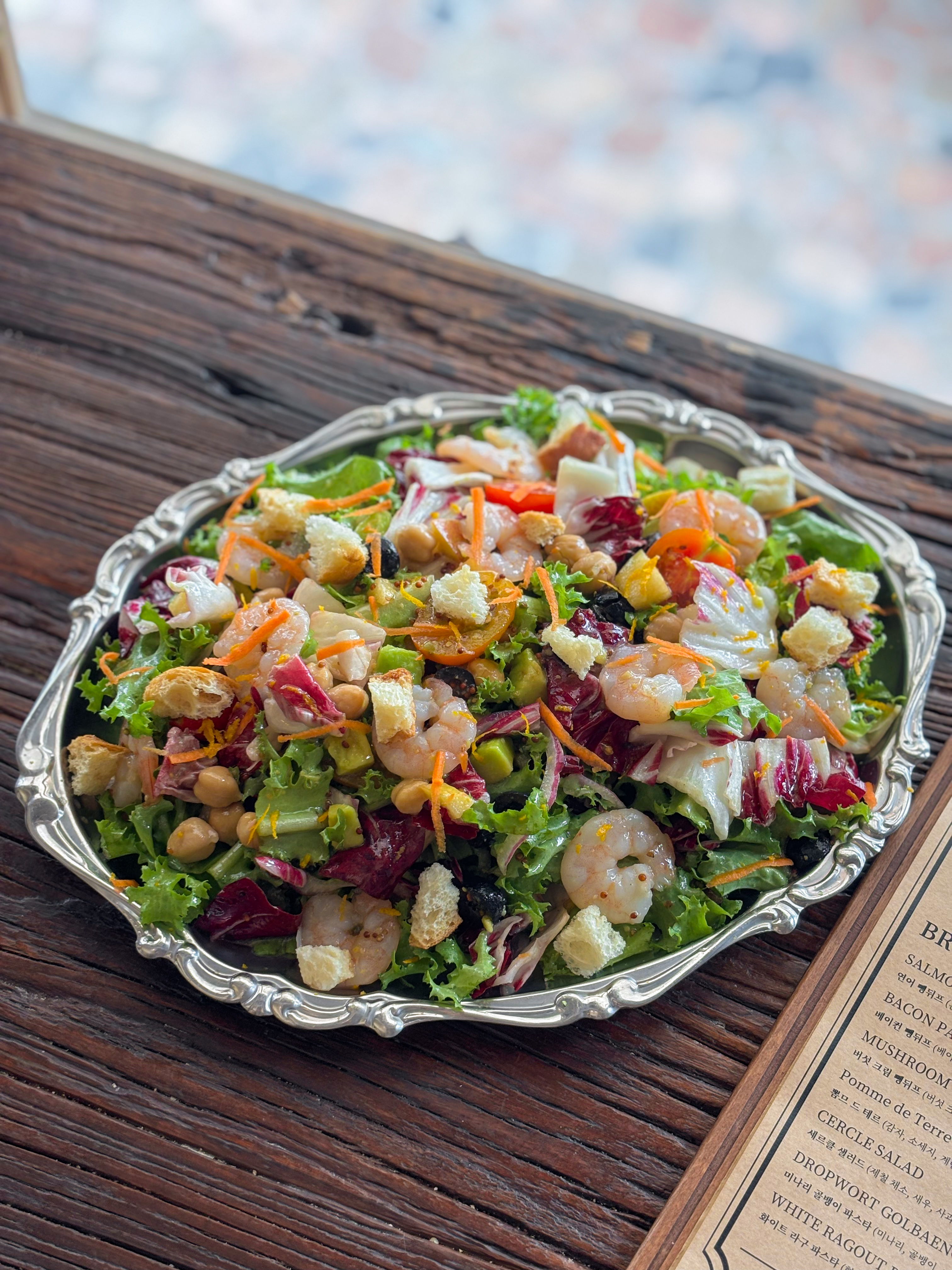 A fresh shrimp salad served on a decorative silver platter on a dark wood table.