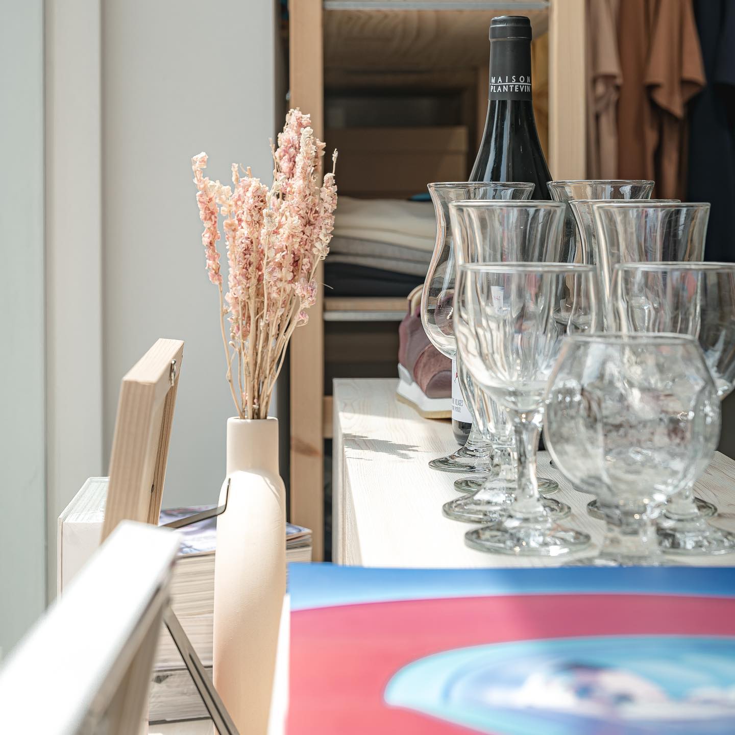A close-up view of wine glasses, a wine bottle, and a vase with dried flowers on a shelf in a shop interior