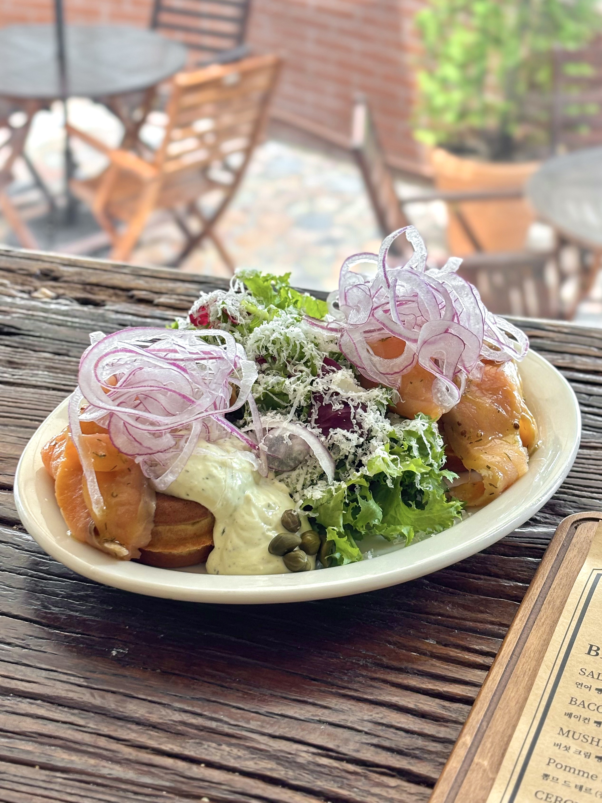 A gourmet salmon brunch dish with salad, capers, and red onion on a weathered wooden table.