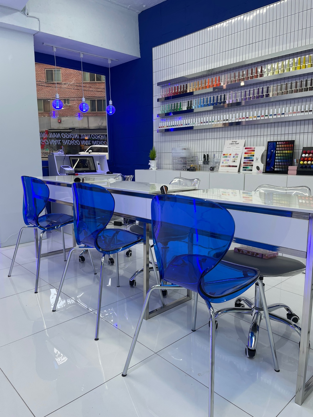 Interior of modern nail salon featuring bright blue transparent chairs and polish shelves