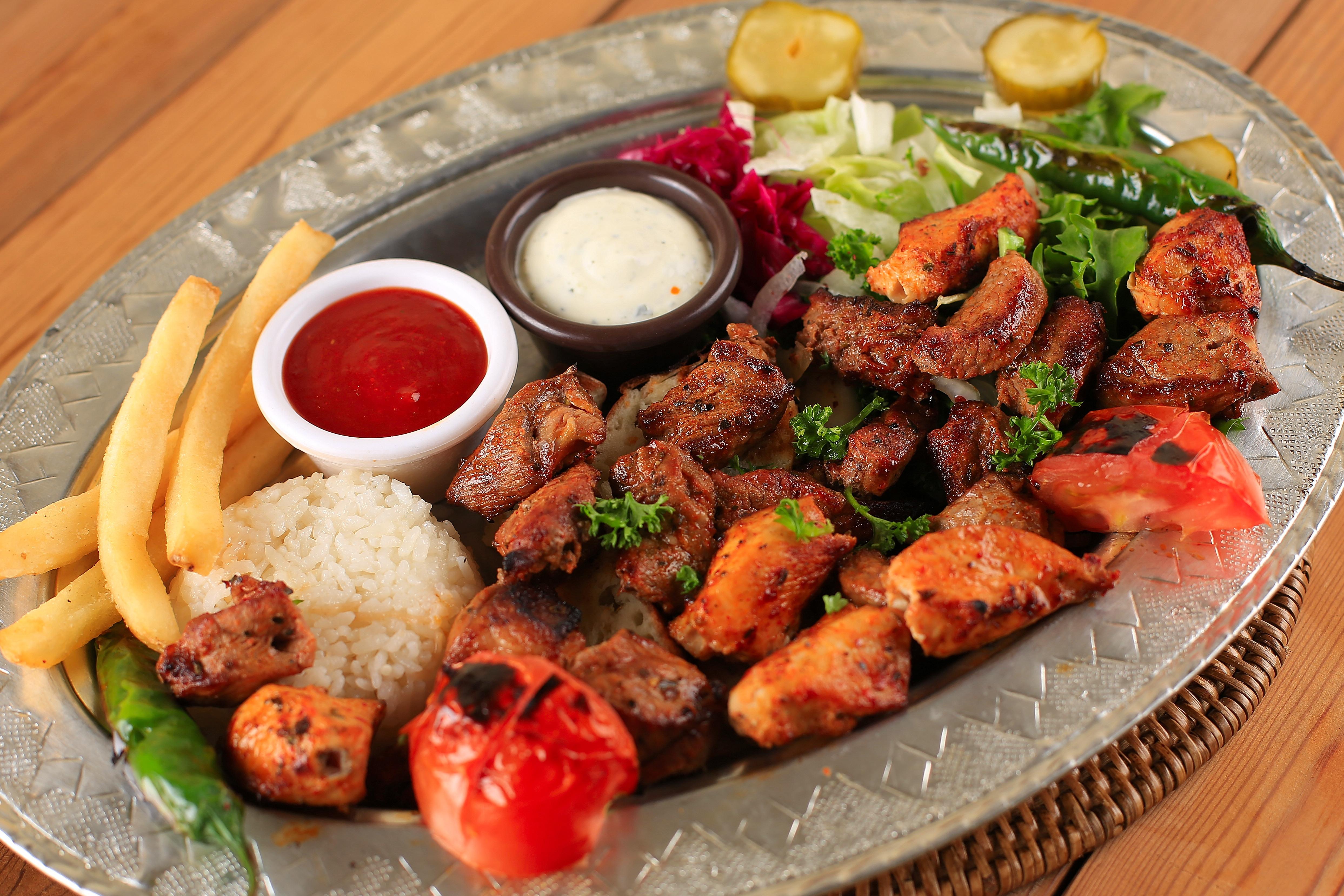 A metal platter serving grilled meat skewers, rice, french fries, vegetables, and two sauces at Kervan Restaurant.