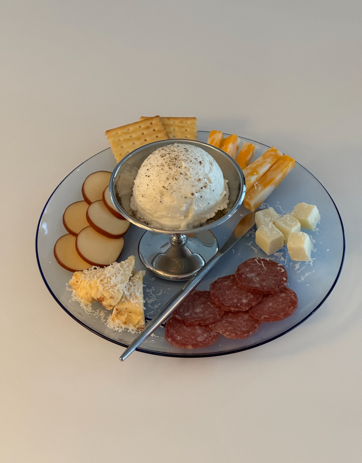 Curated charcuterie plate with cheese, crackers, salami, and whipped cheese cream on translucent glass dish