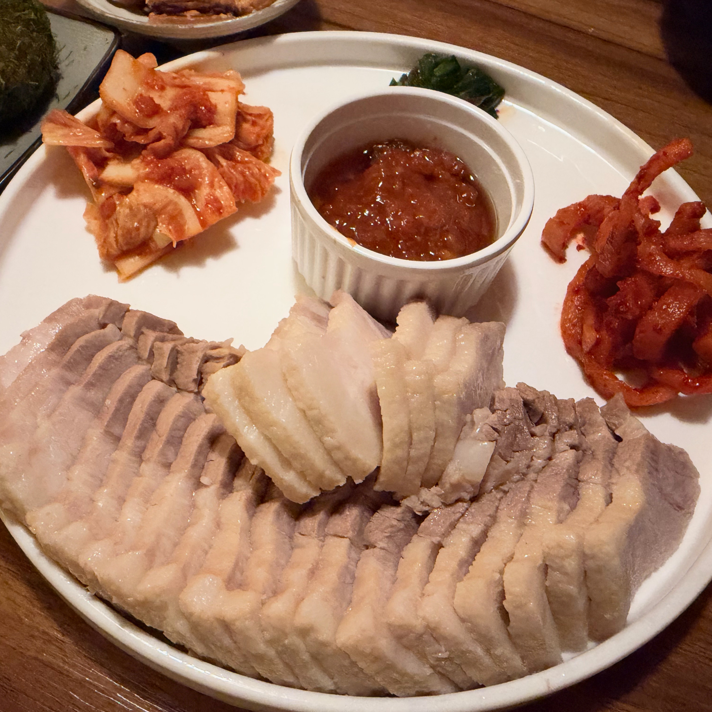 Bossam pork platter served with kimchi, spicy radish salad, and chili dipping sauce