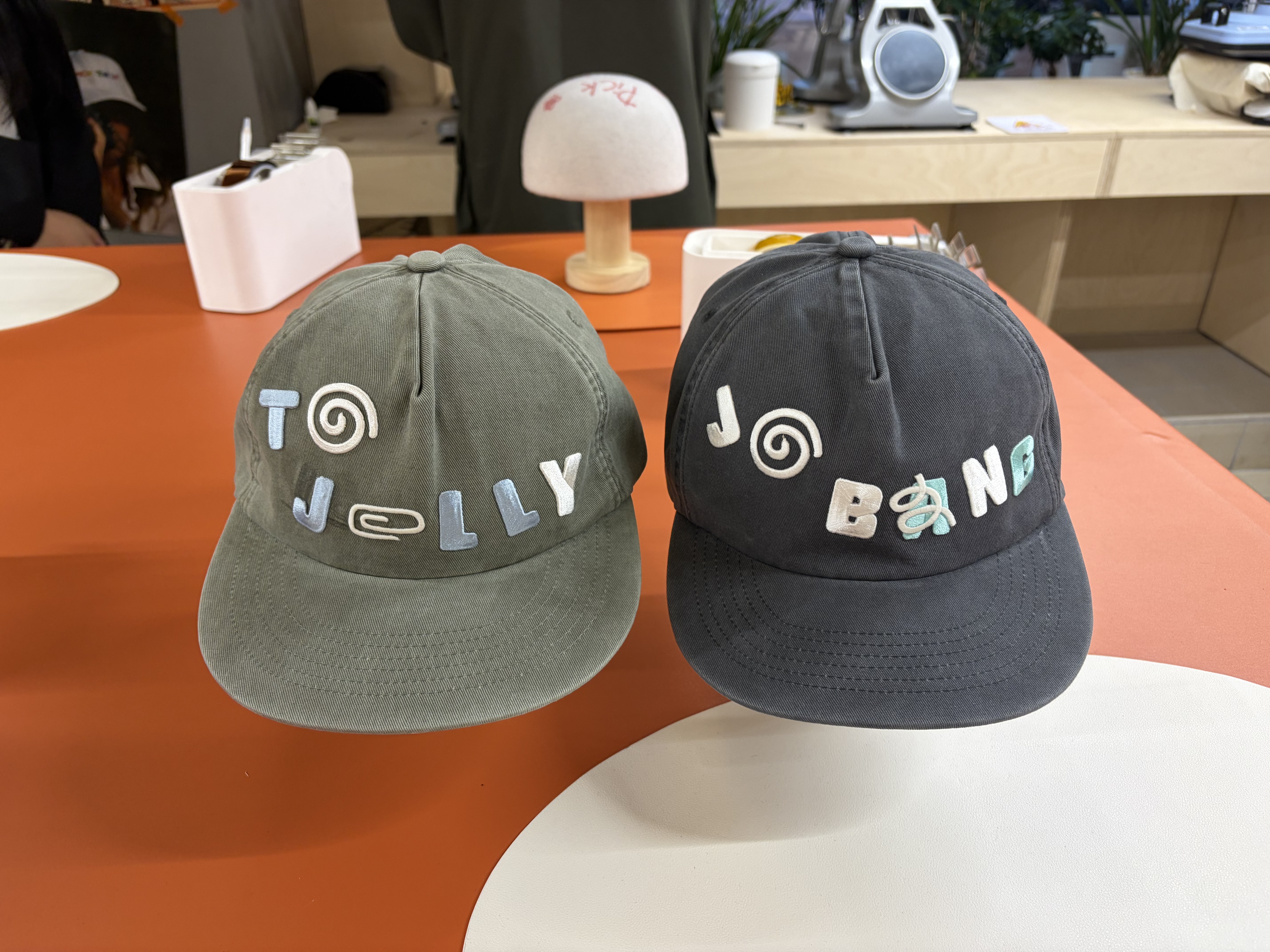 Two finished embroidered baseball caps displayed on stands inside the Yeonnam workshop