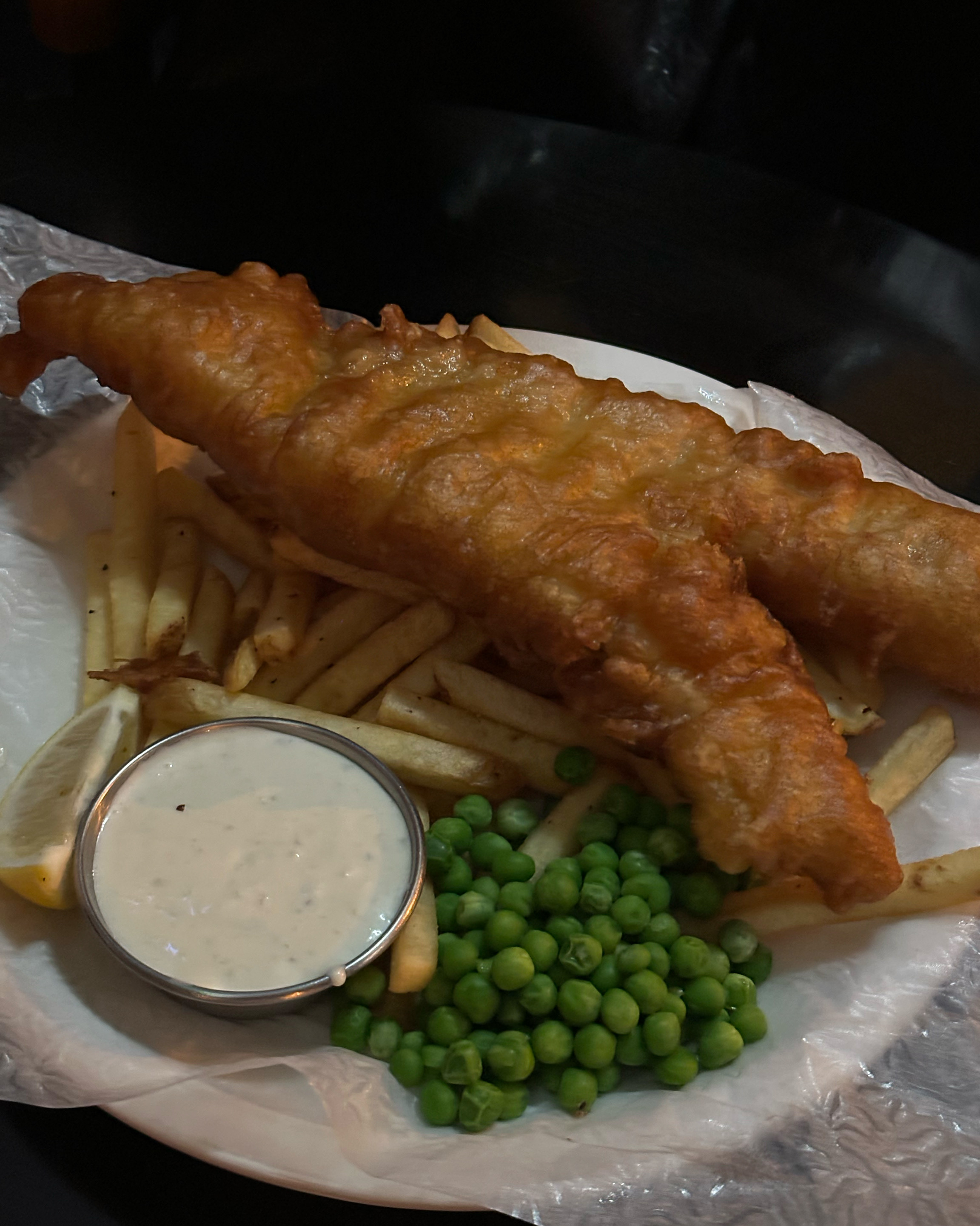 Close-up of fried fish fillet with french fries, lemon wedge, and dipping sauce