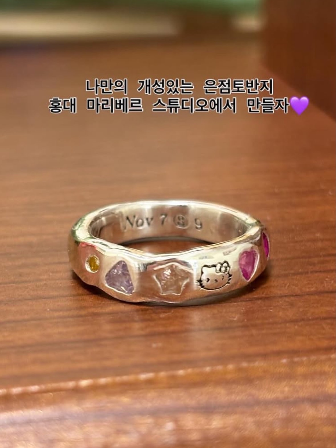 A silver ring with embedded charms resting on a brown wooden surface.