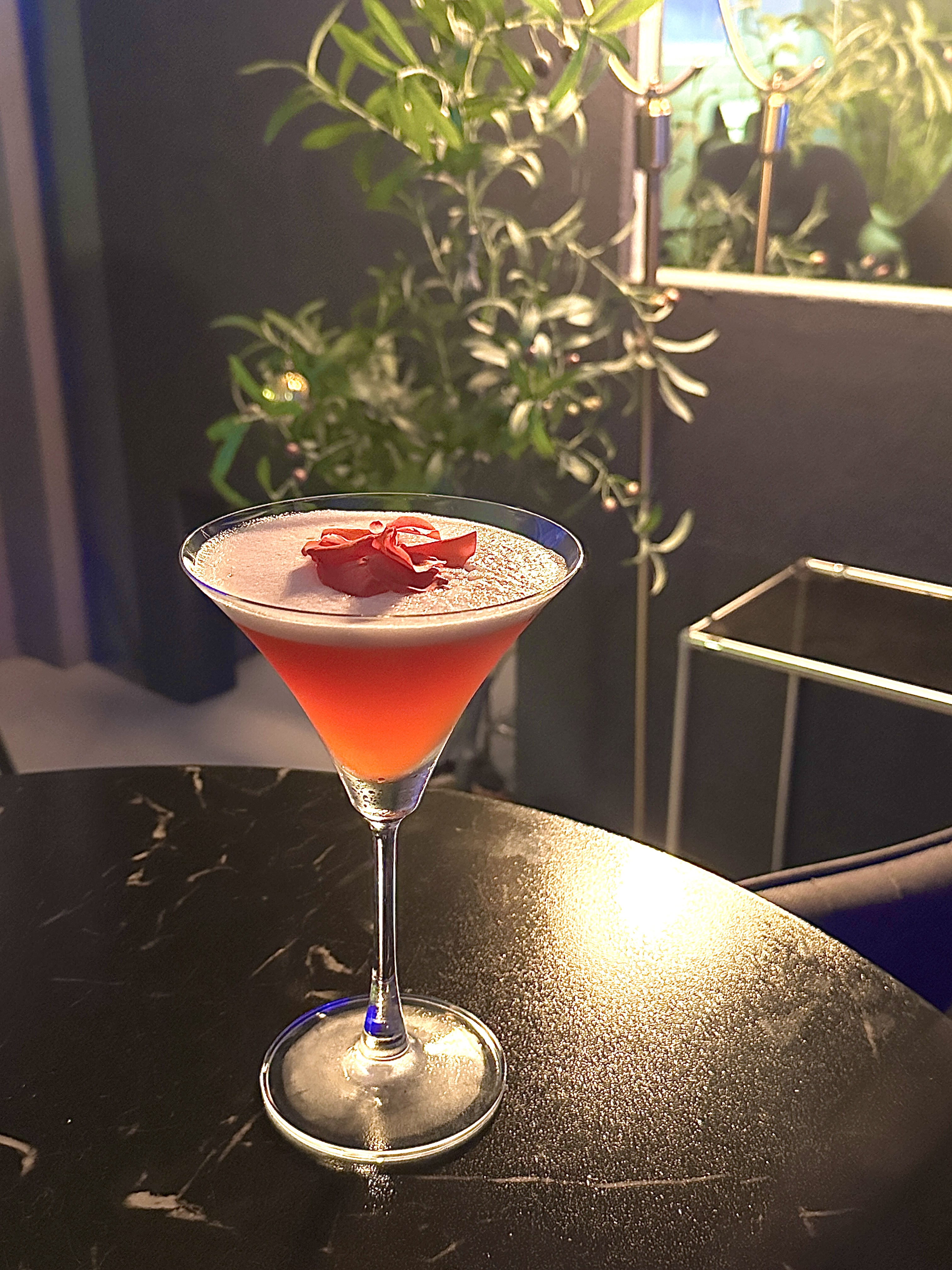 Pink martini cocktail garnished with rose petal on black veined marble table