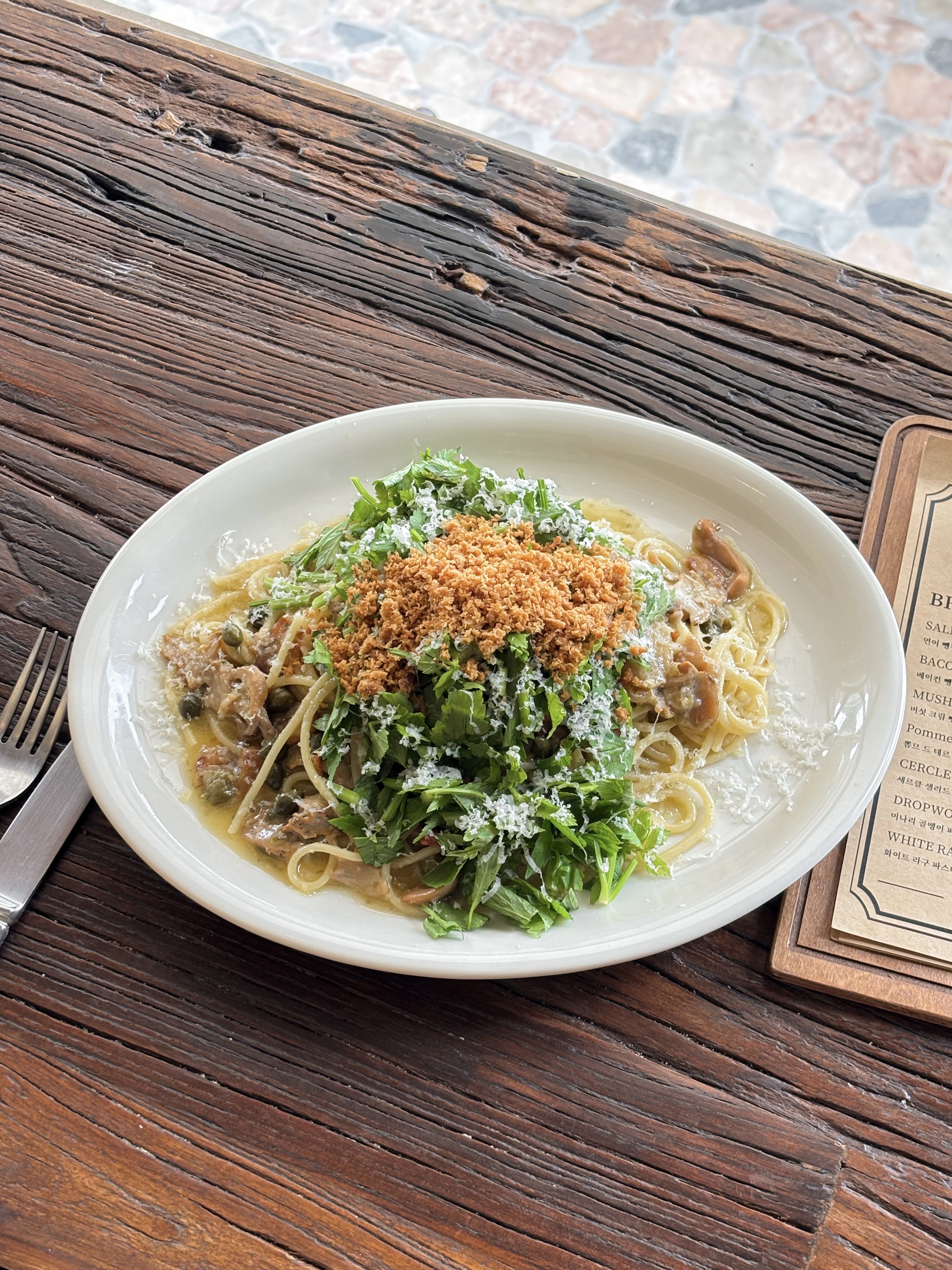 A plate of pasta topped with green herbs and toasted crumbs on a rustic wooden table.