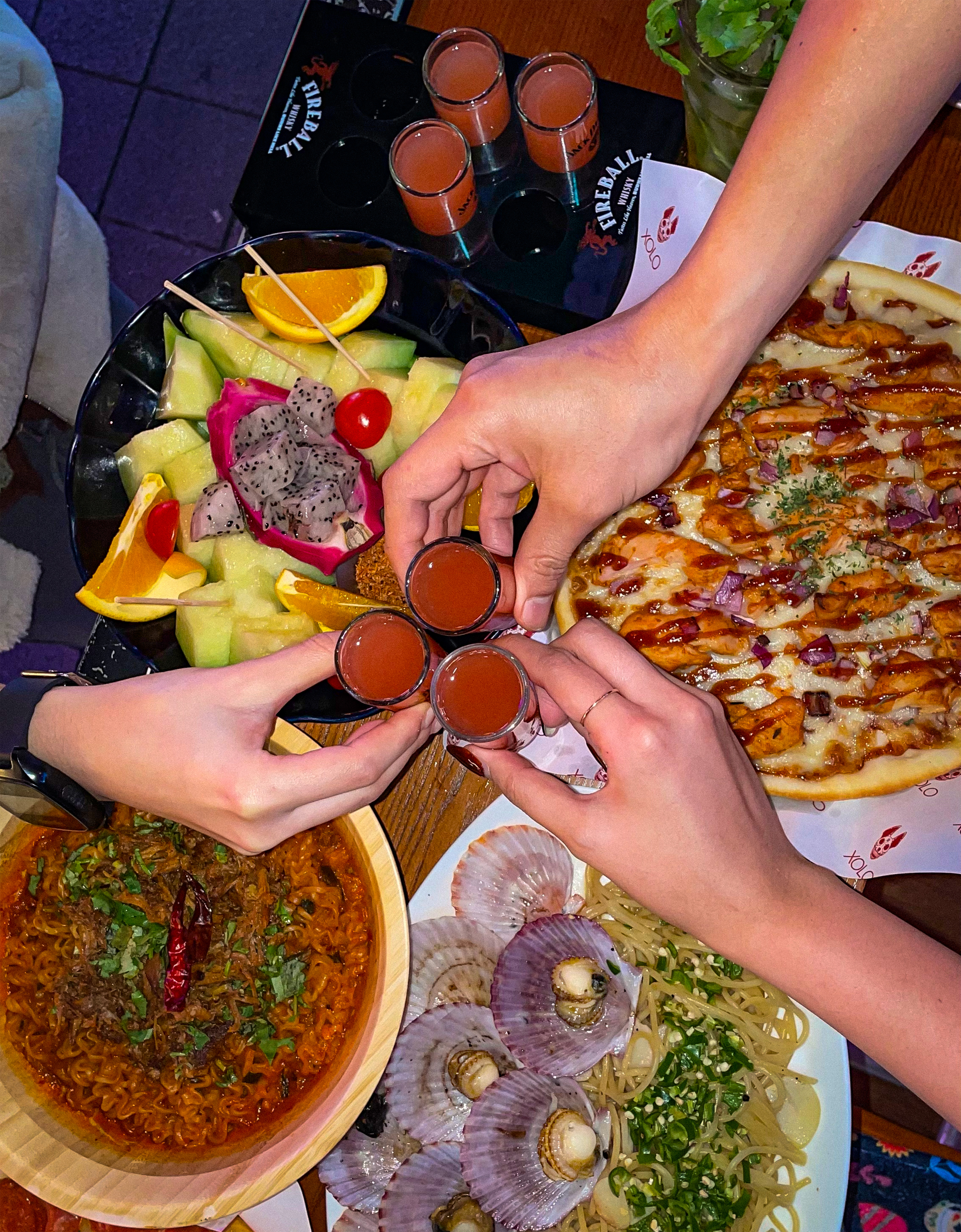 Dining table with assorted Mexican dishes, noodles, pizza, and group toast