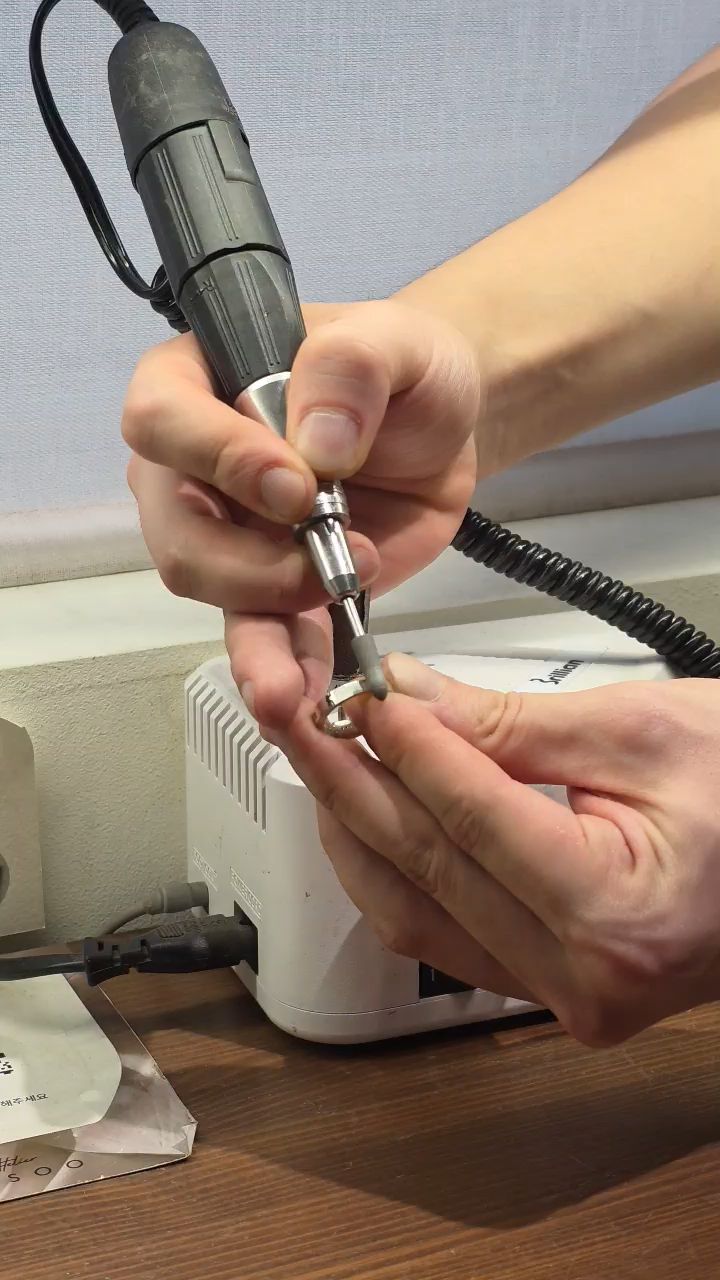 Hands using a rotary tool to polish a small silver ring at a craft workbench