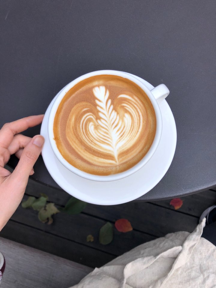 A cup of latte with leaf latte art sitting on a dark grey table