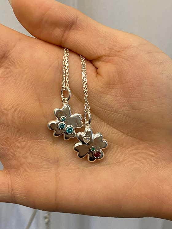 Two silver clover-shaped pendants with colorful inset gemstones held in palm