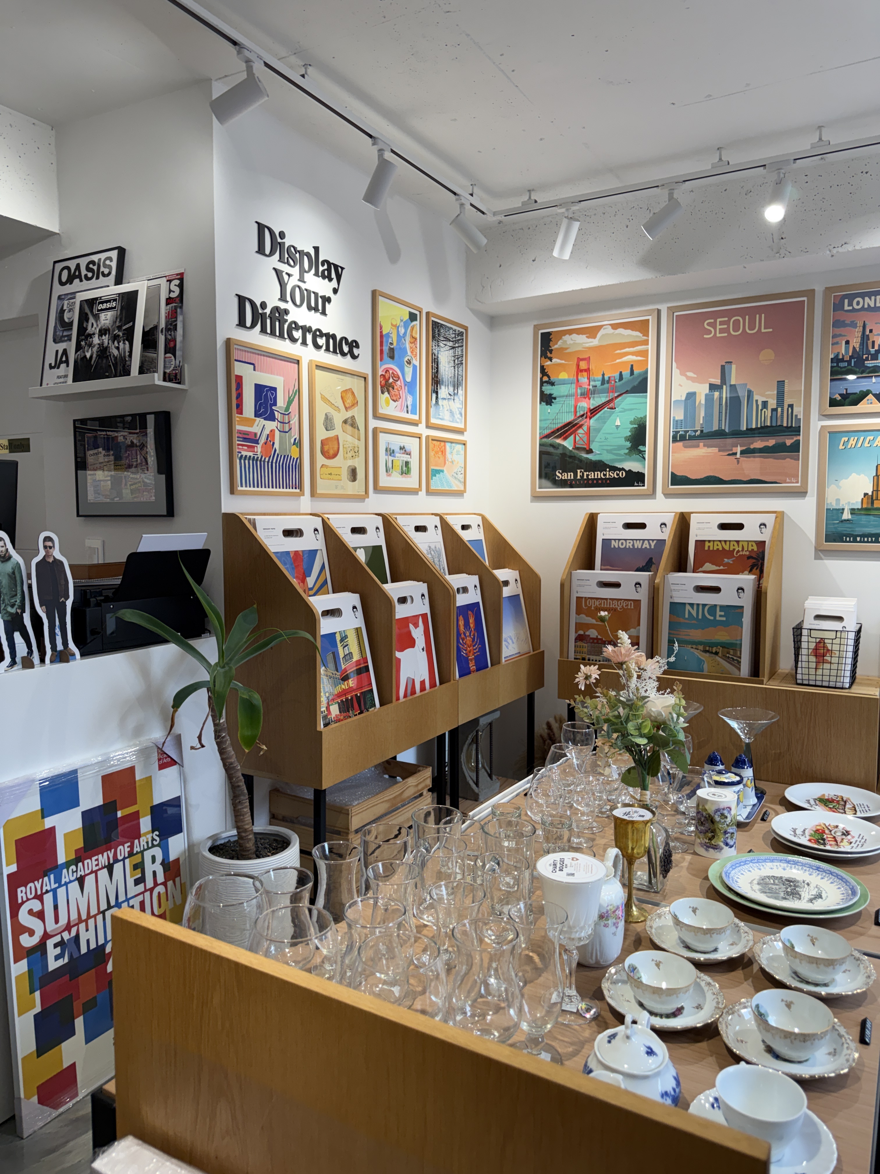 Interior of Bank Holiday interior decor shop displaying posters, teacups, and glassware on wooden shelves and tables