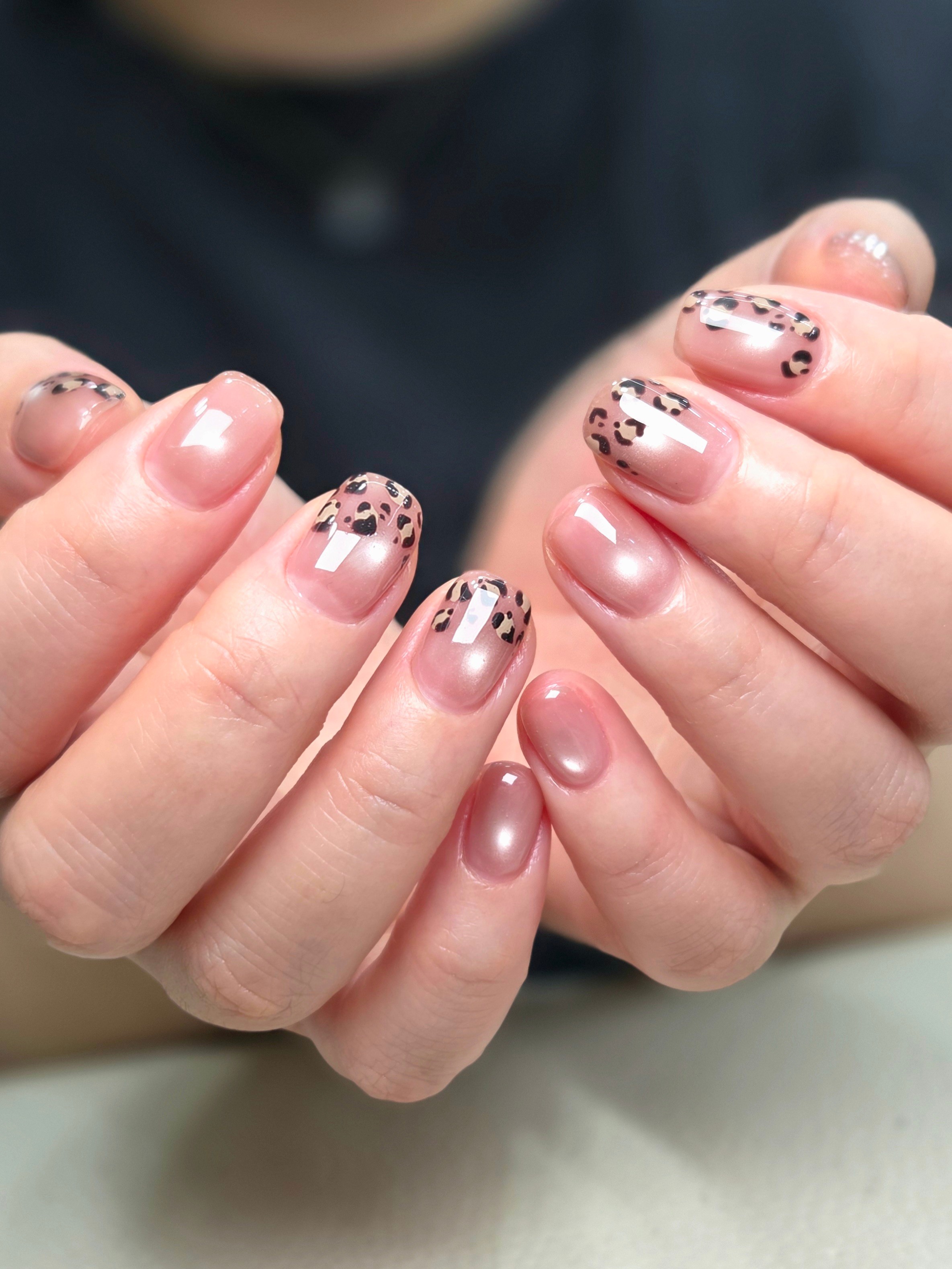Close-up of hands with manicured nails featuring a clear nude base and leopard print designs on the tips