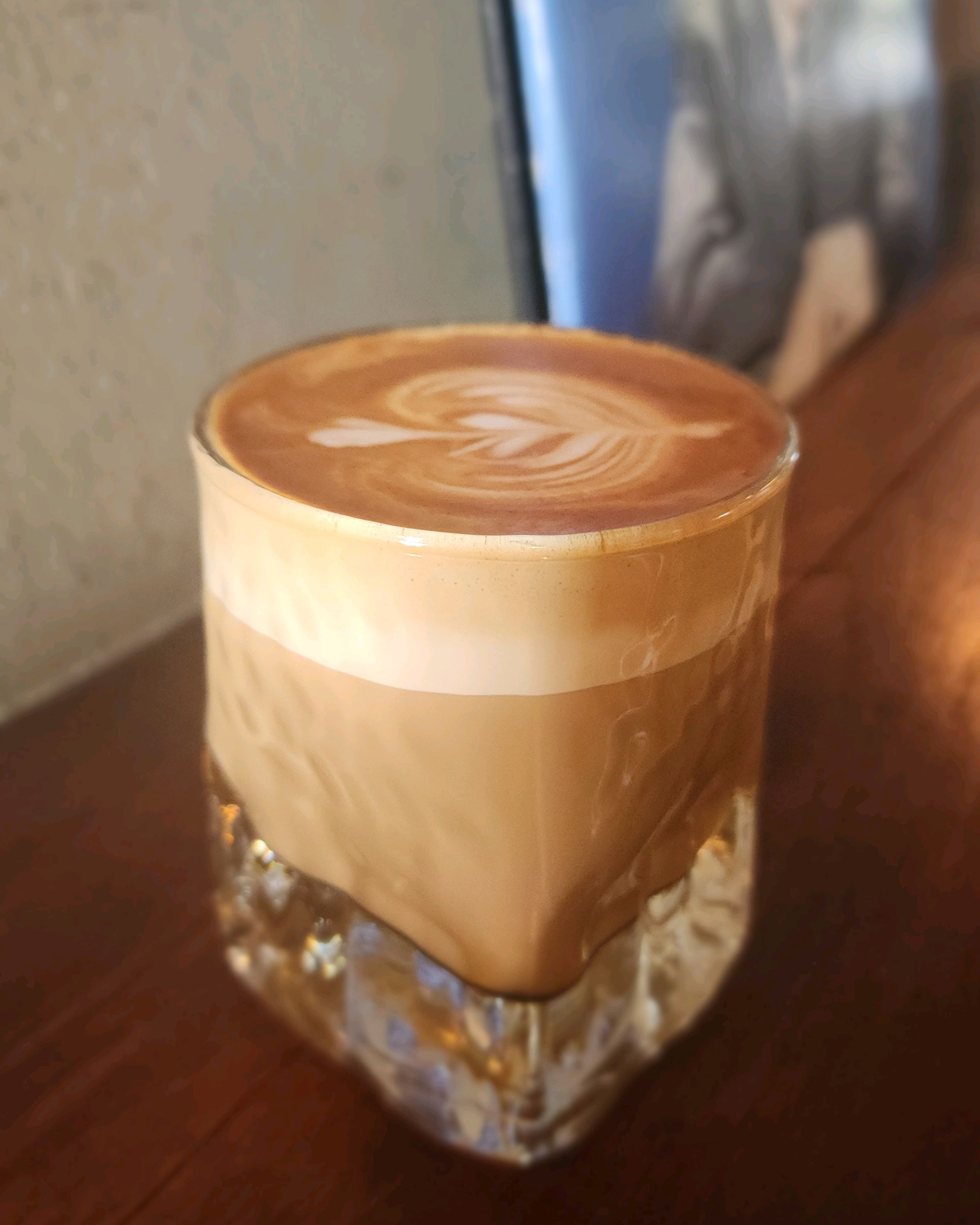 Layered flat white coffee with latte art served in a faceted glass.