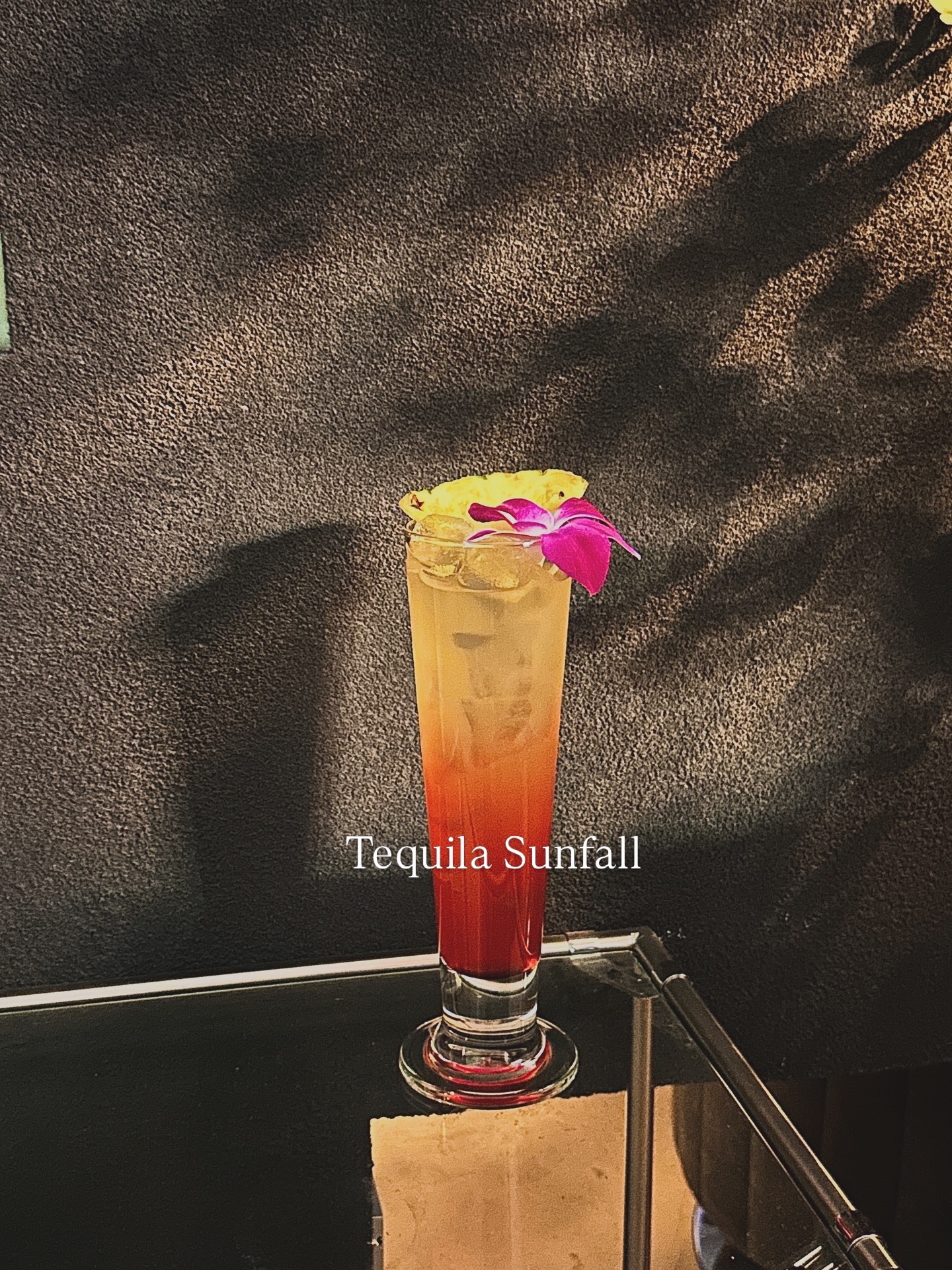 Layered Tequila Sunfall cocktail garnished with pineapple and purple orchid