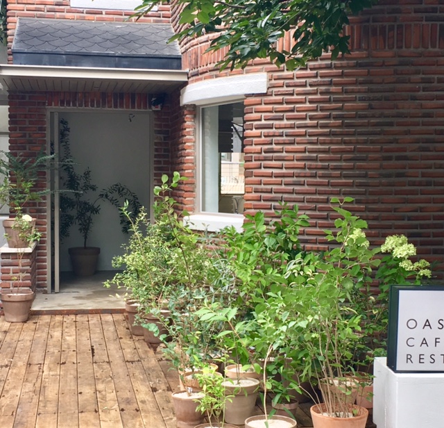 Exterior entrance of Oasis Hannam featuring red brick walls, wooden decking, and various potted plants