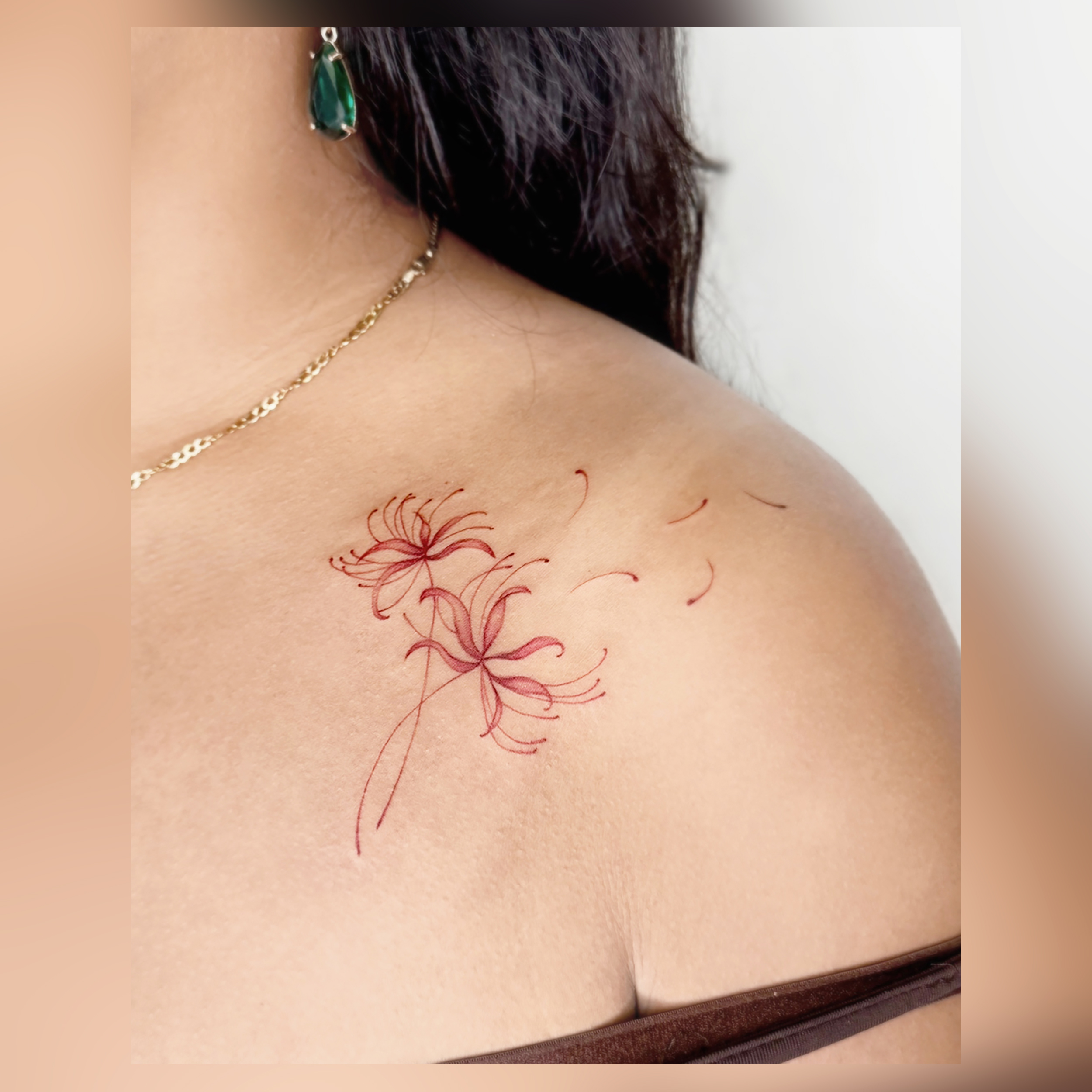 Delicate red ink spider lily tattoo on shoulder