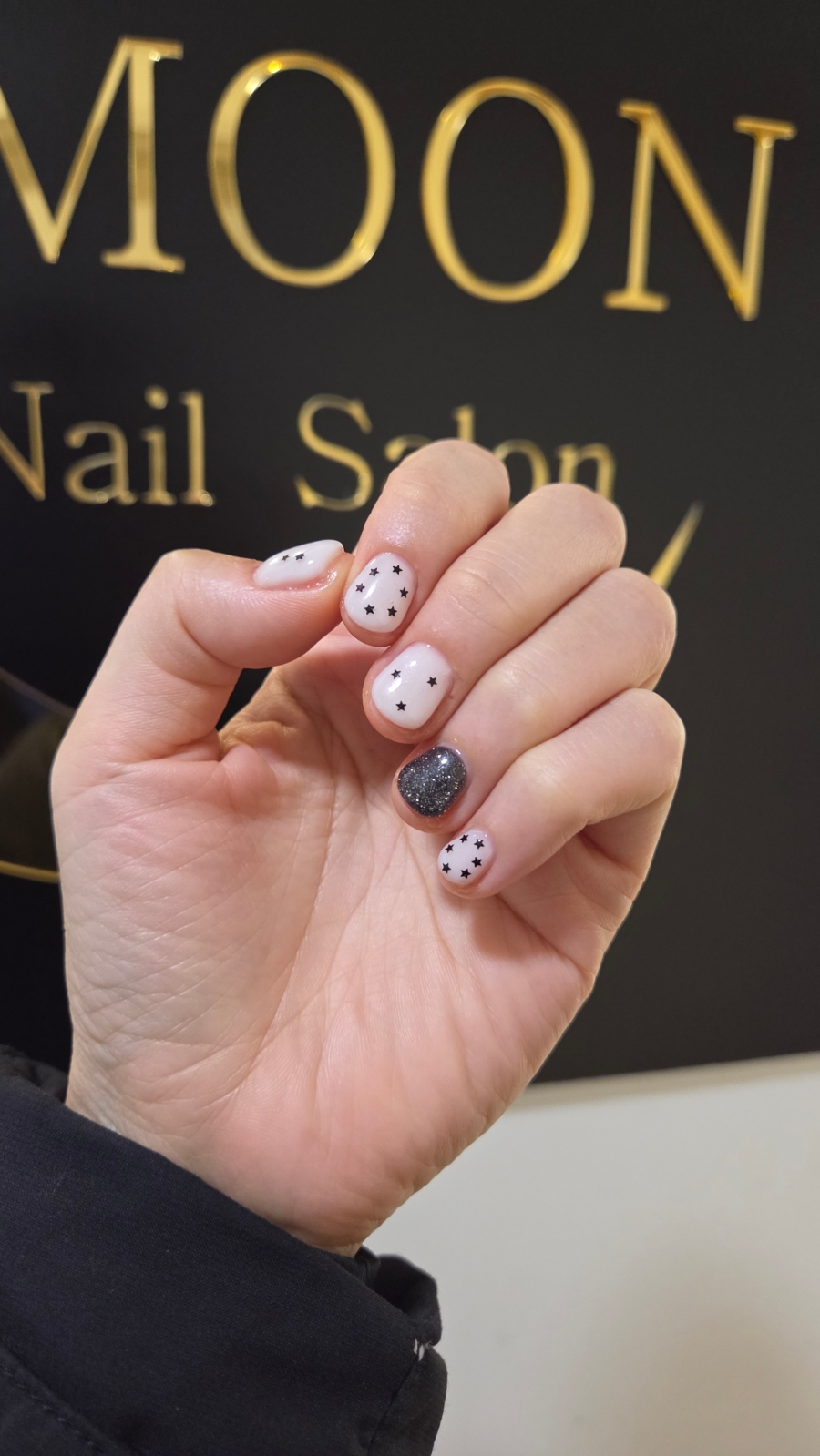 Close-up of fingernails with white base, black star designs, and dark glitter accent