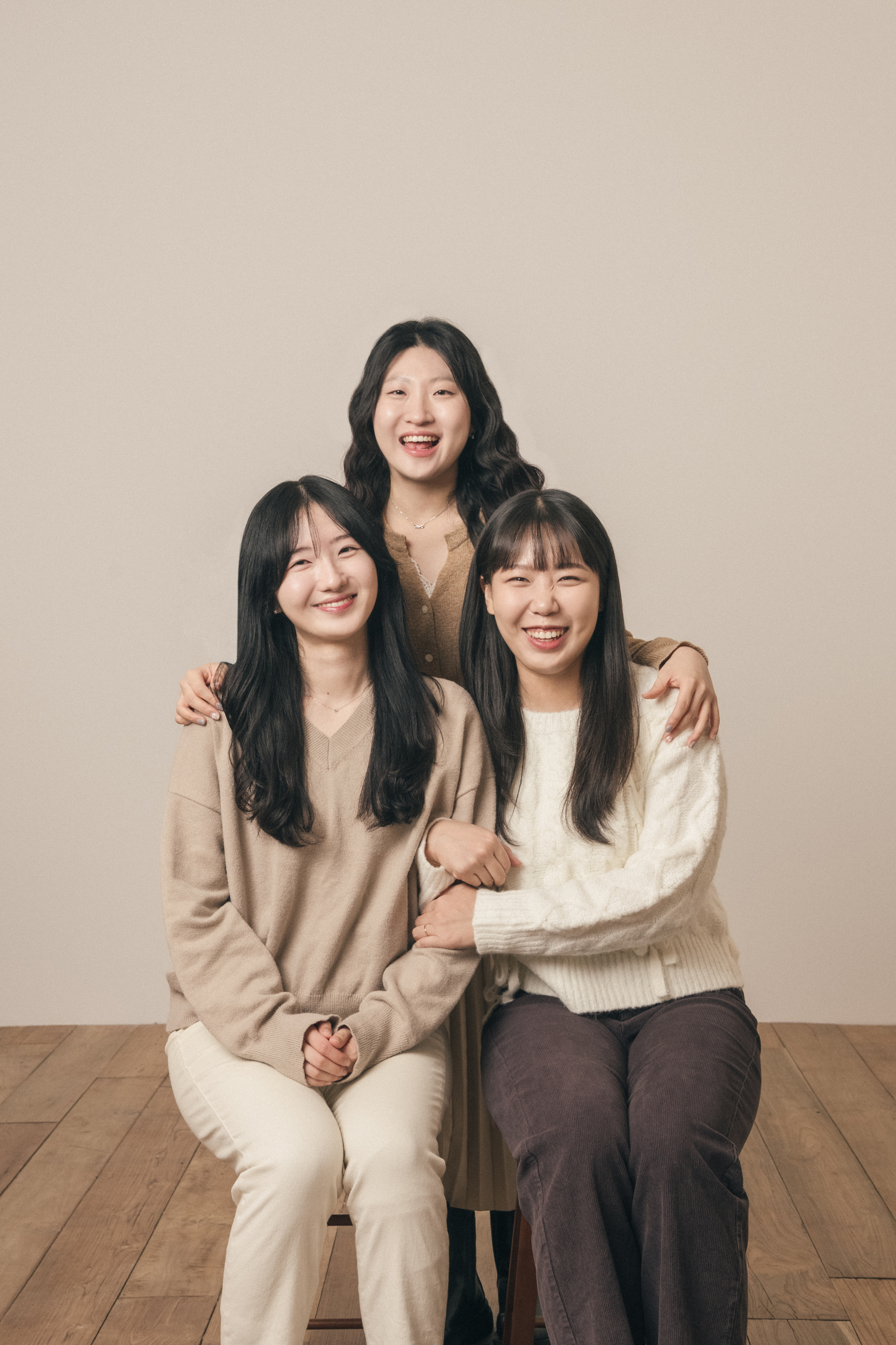 Three smiling women posing for a professional studio portrait against a neutral beige background