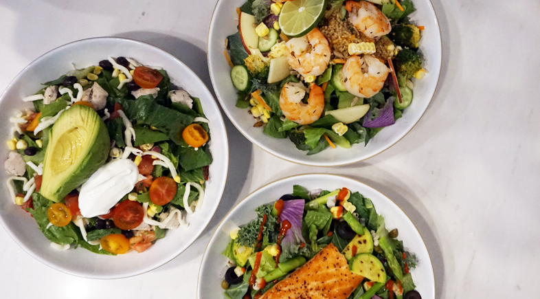 Three diverse salad bowls with shrimp, salmon, and avocado on marble surface