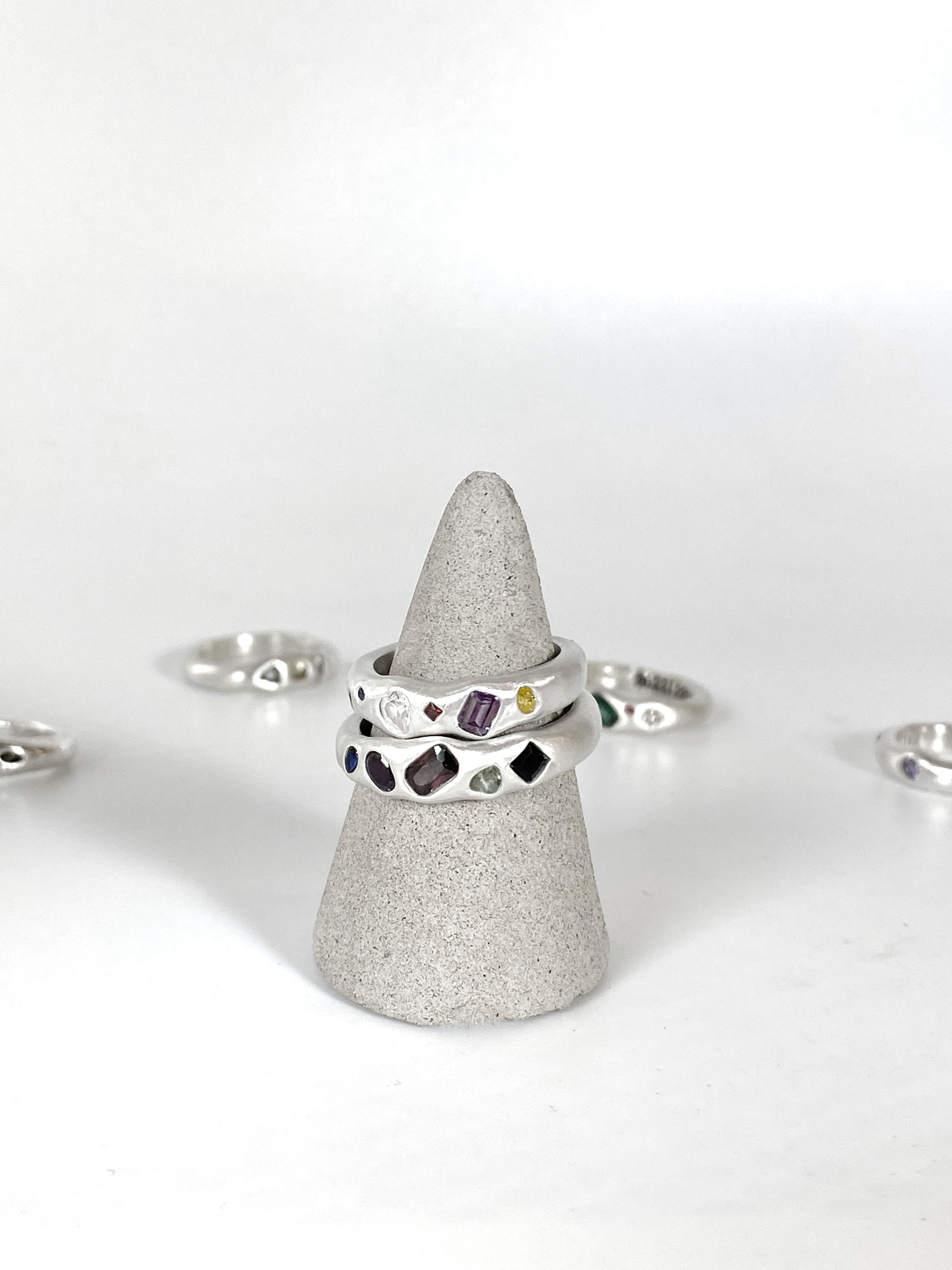Stacked handcrafted silver rings with embedded colorful gemstones on concrete display cone