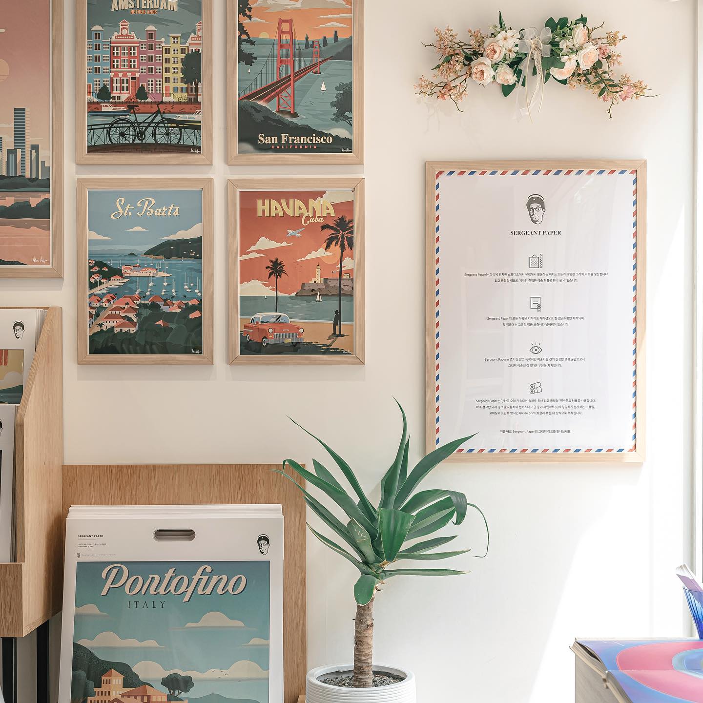 A gallery wall featuring framed travel posters and an informational document, with an indoor plant below