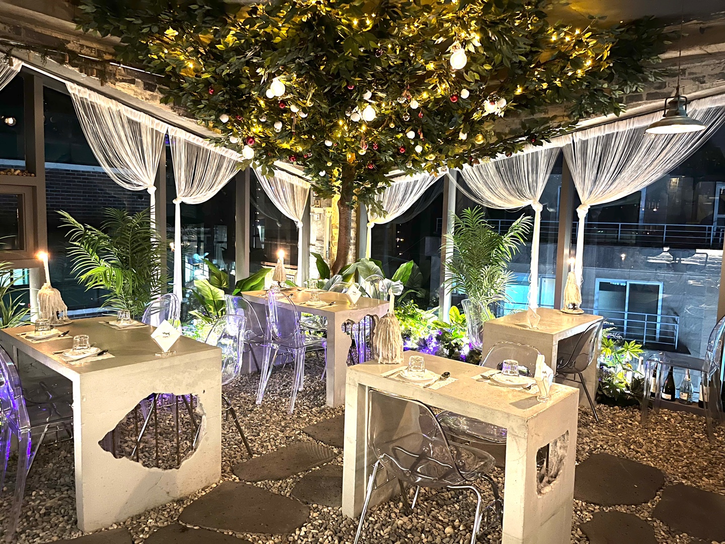 Interior dining space featuring modern stone tables, grey pebble flooring, and an illuminated central tree