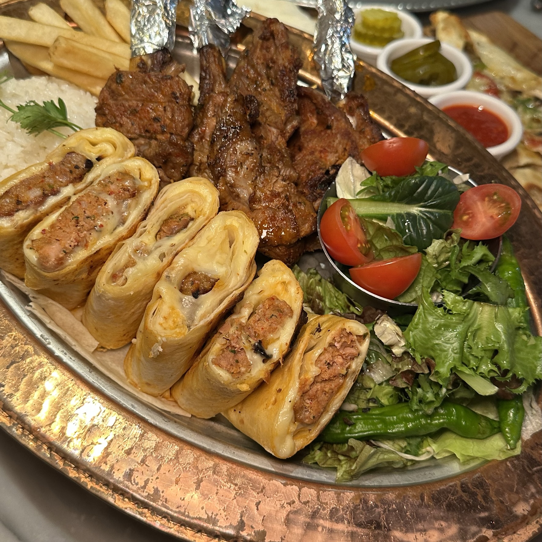 A platter featuring grilled lamb chops, meat-filled wraps, French fries, rice, and a side salad.