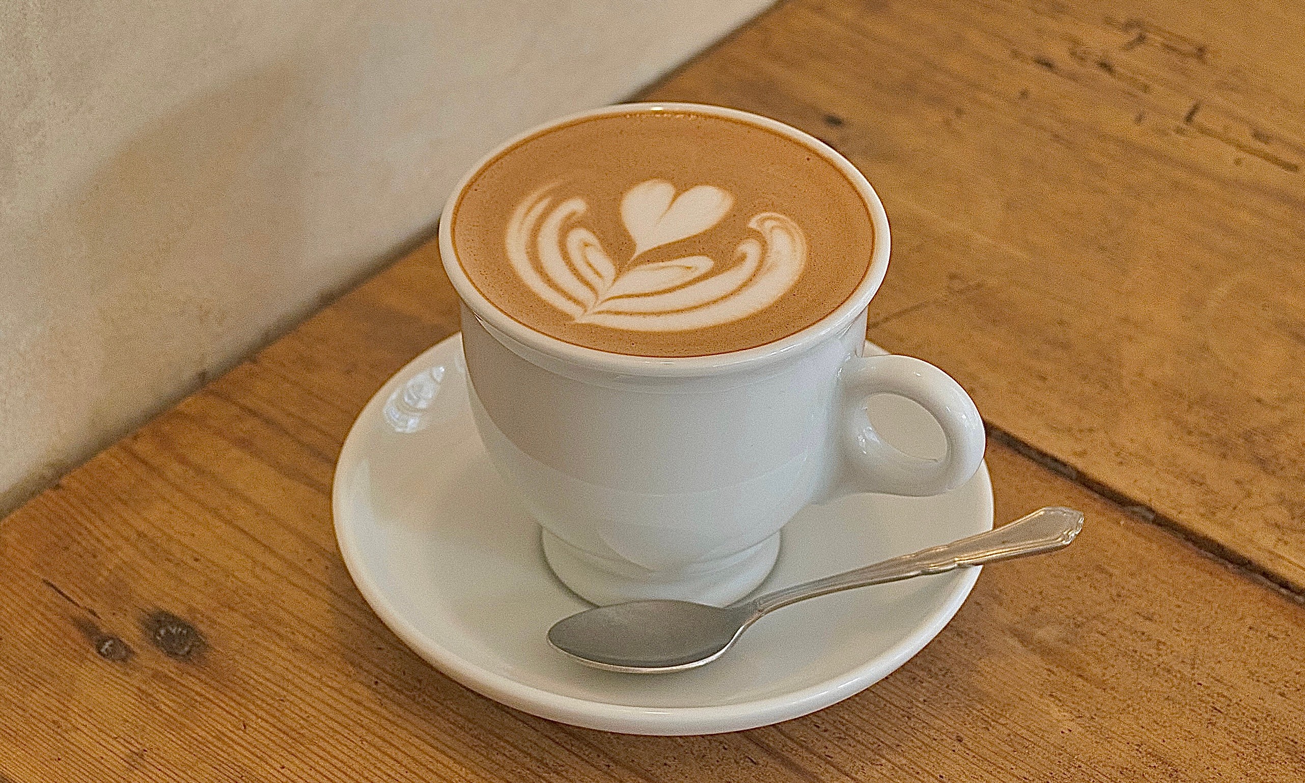 Freshly poured latte with delicate heart foam art on a wooden cafe tabletop
