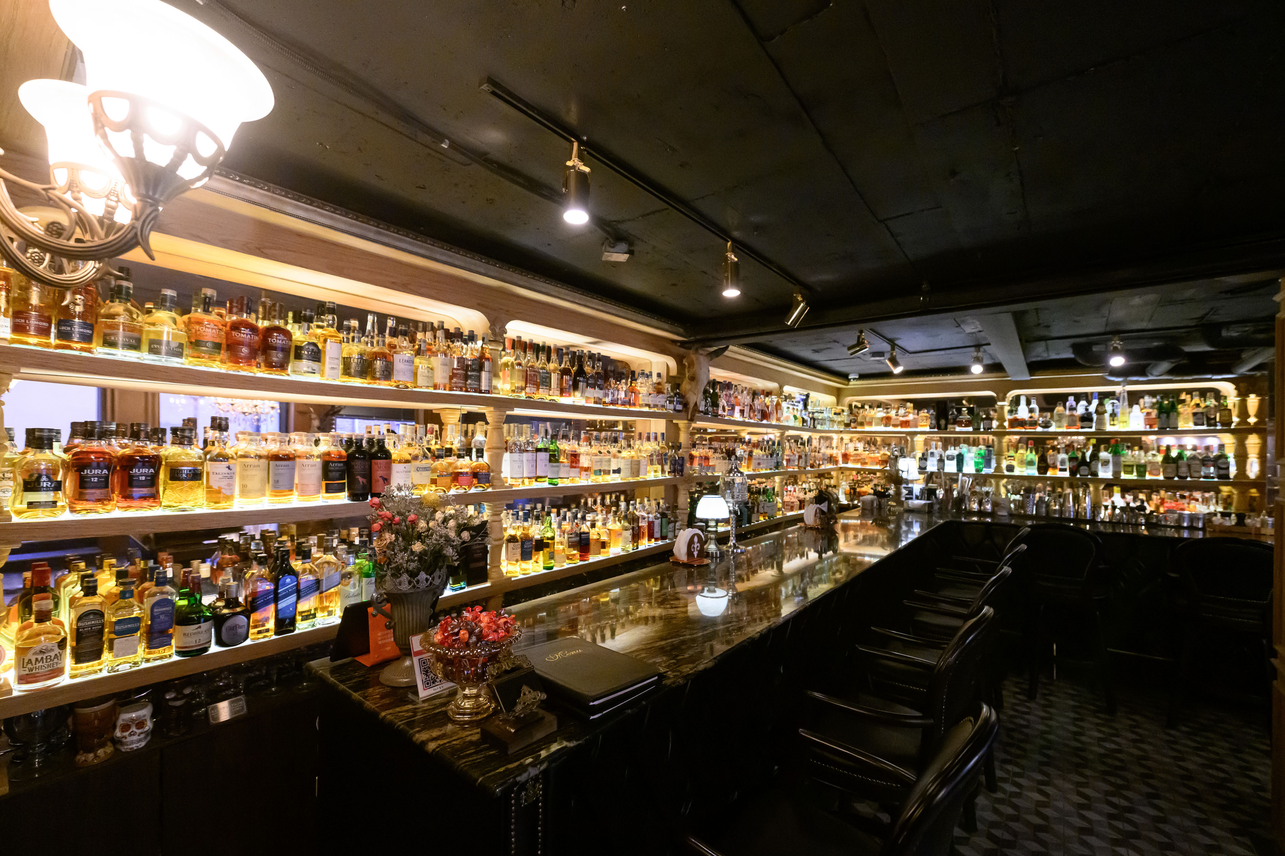 Long dark marble bar counter with leather stools and backlit bottle shelves