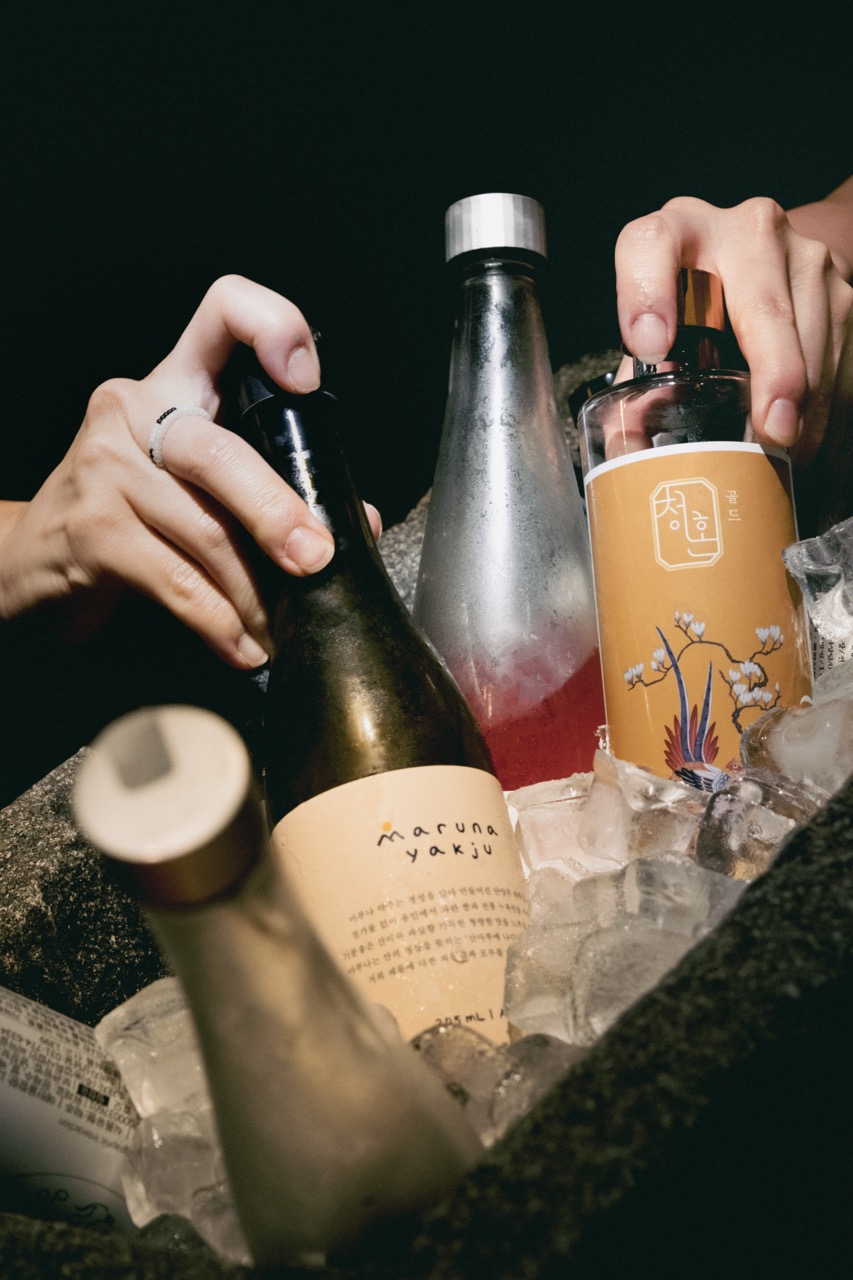 Several glass liquor bottles with labels chilling in a dark stone ice bucket.