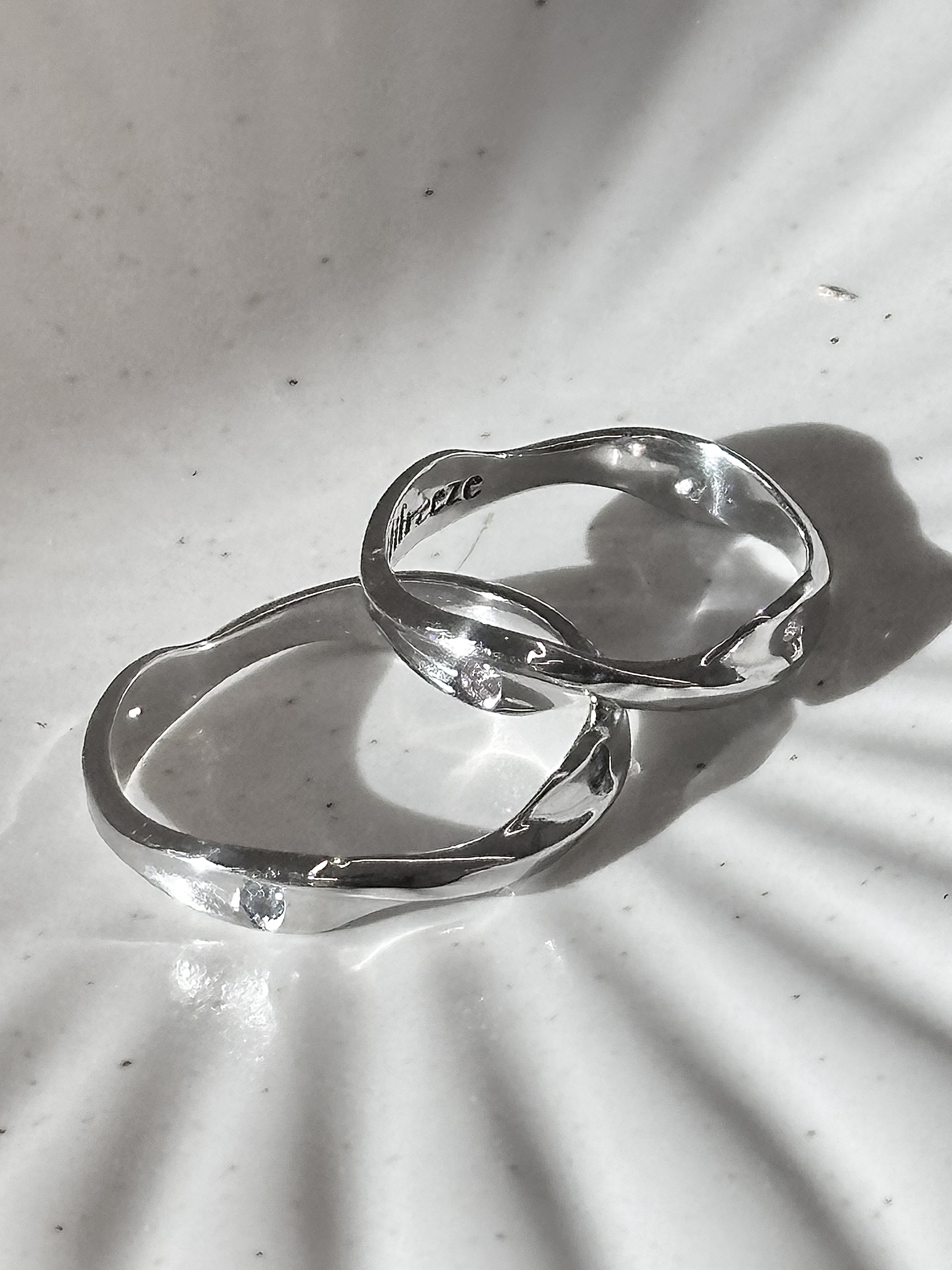 Two polished silver rings with organic, wavy edges resting on a white, textured surface