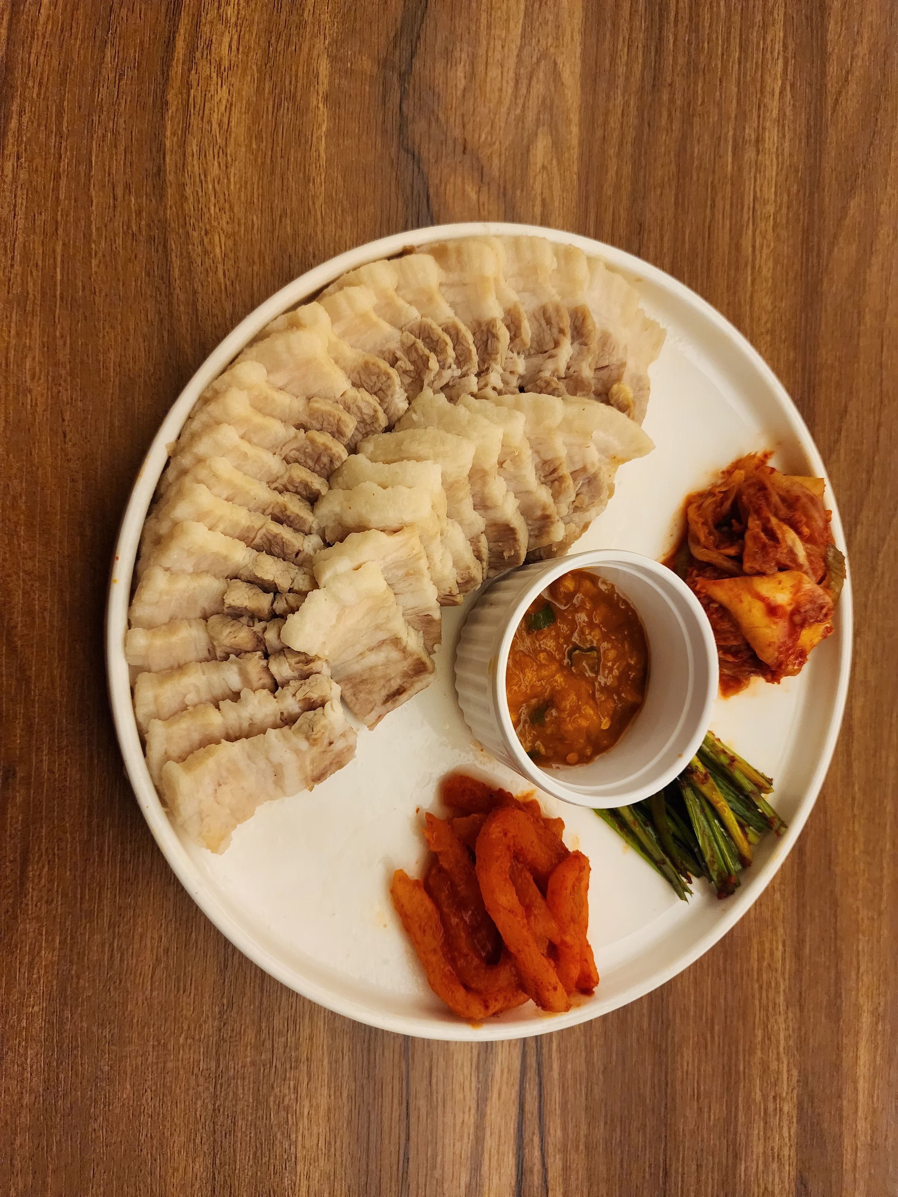 Thinly sliced boiled pork belly served with spicy seasoned radish strips, kimchi, and dipping sauce