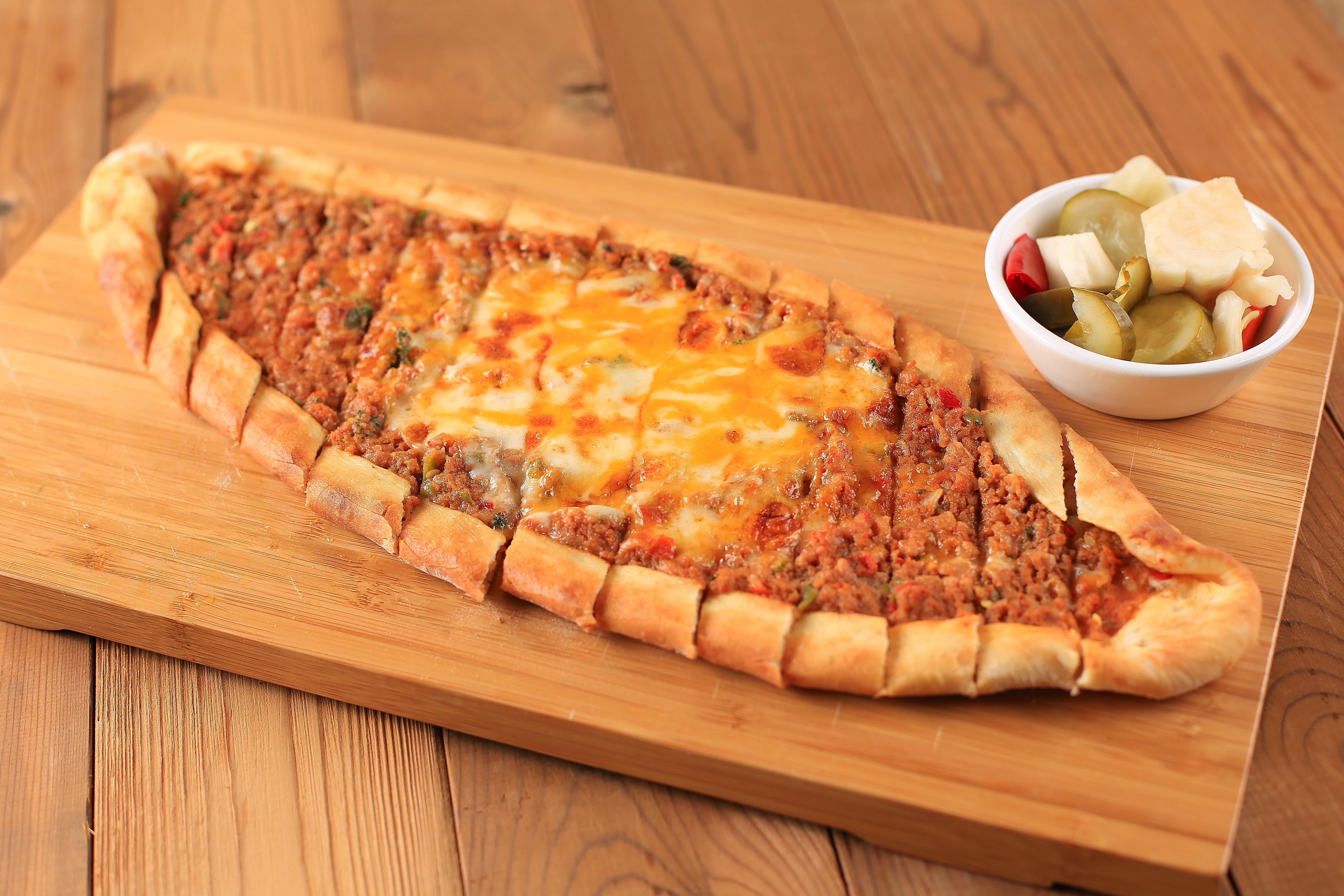 A long Turkish pide topped with meat and cheese served on a wooden board.