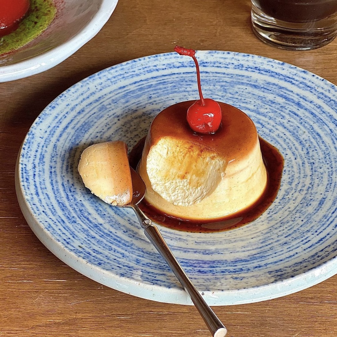 Caramel custard pudding topped with a cherry on a blue and white ceramic plate