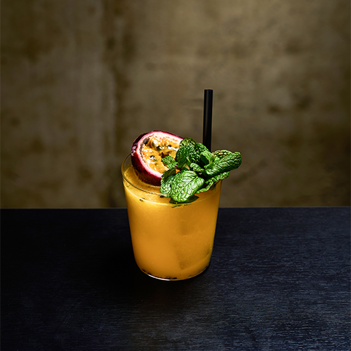 A passion fruit cocktail in a glass with a straw and mint garnish on a dark table.