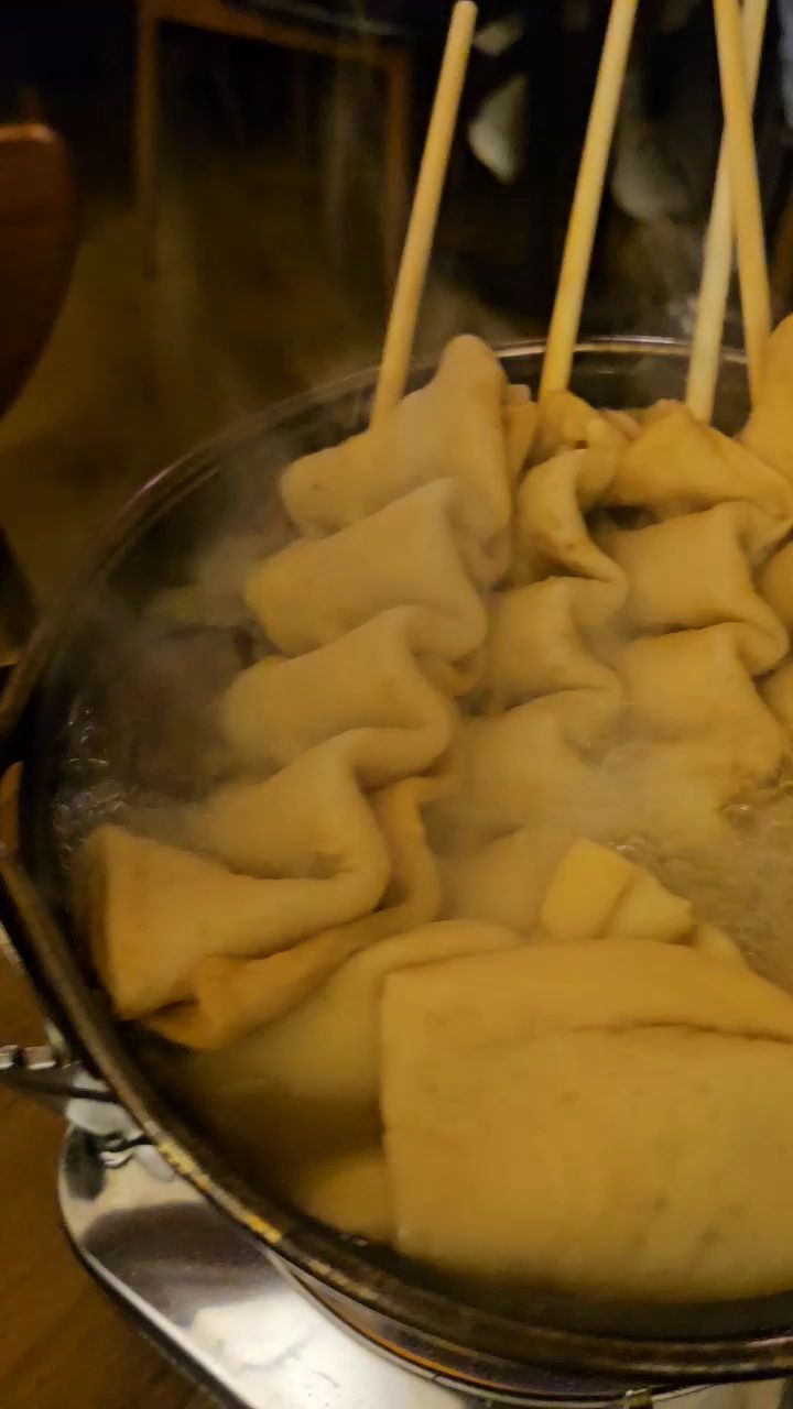 Folded fish cake skewers cooking in simmering savory broth inside a metal pot