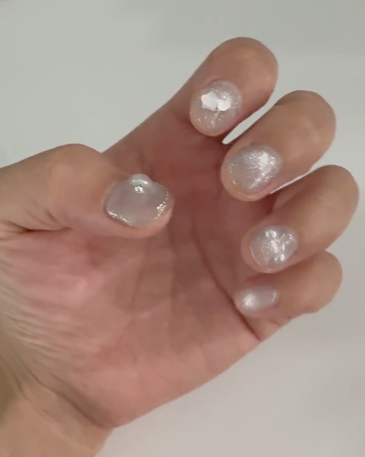 Close-up of hand with sparkly, light-colored nail art featuring small decorative beads