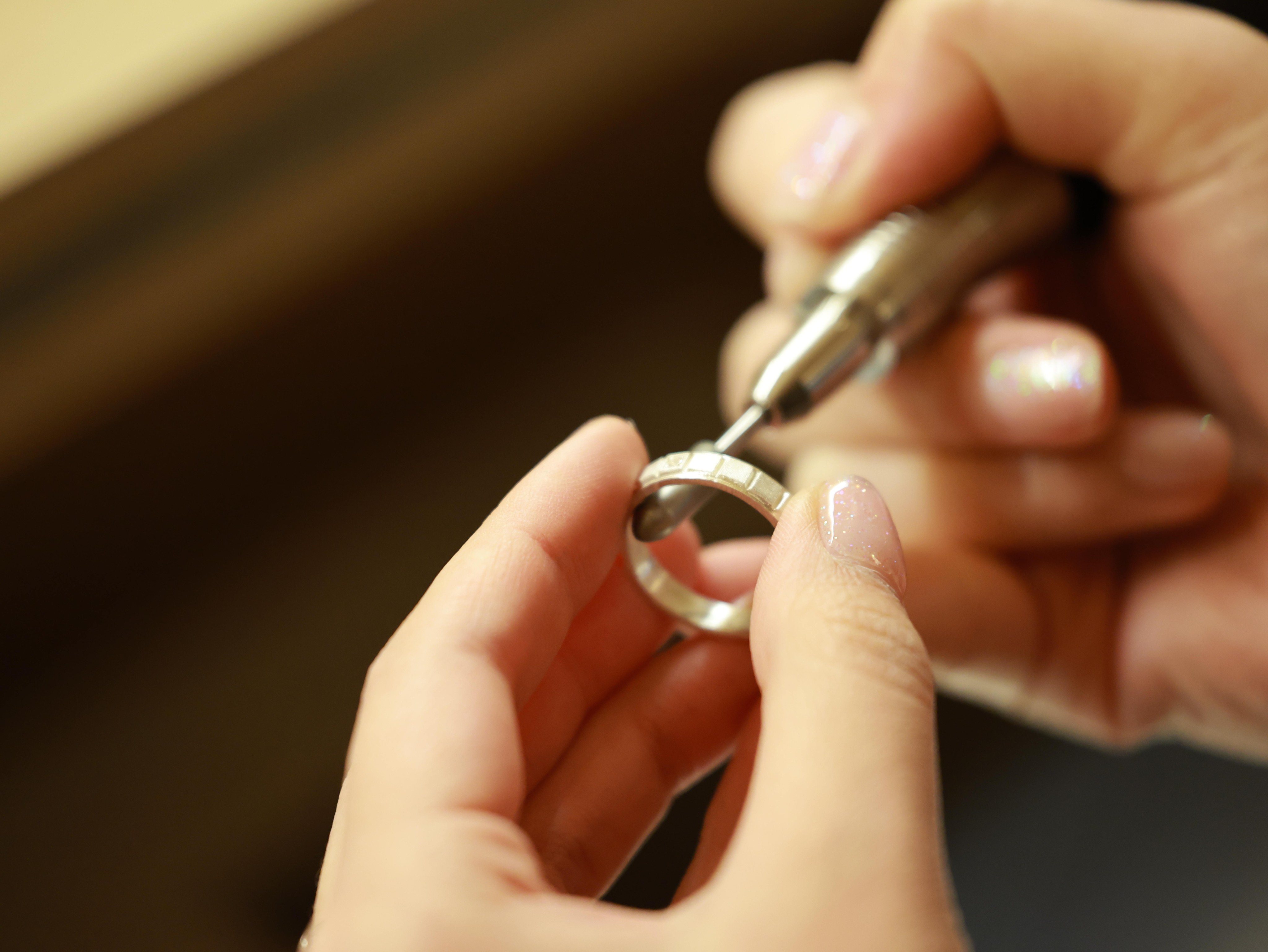 Hands using a rotary burr tool to refine and polish a metallic silver ring